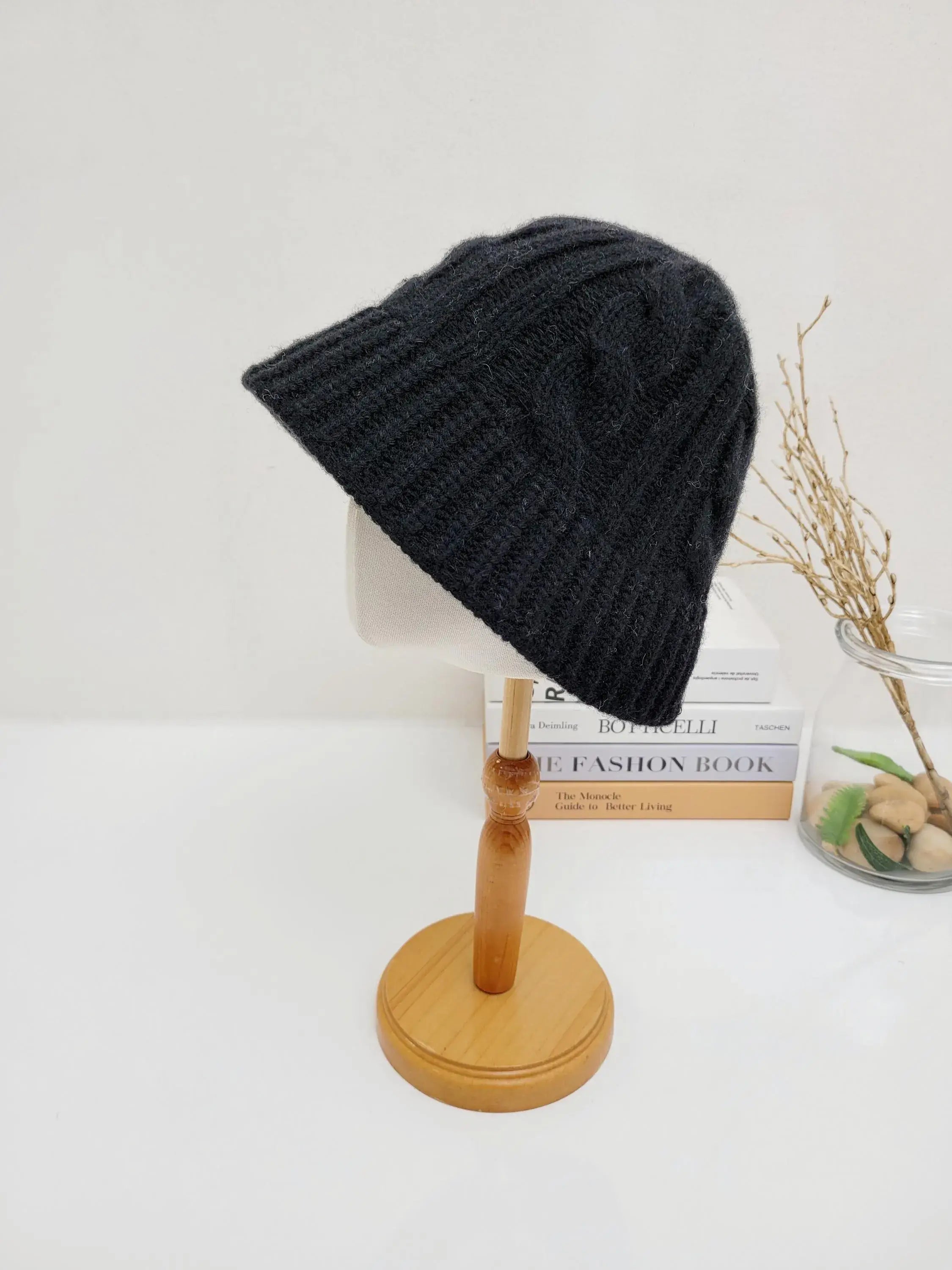 Black cable knit hat on a wooden display stand. Warm and stylish, this cable knit hat is perfect for cold weather.