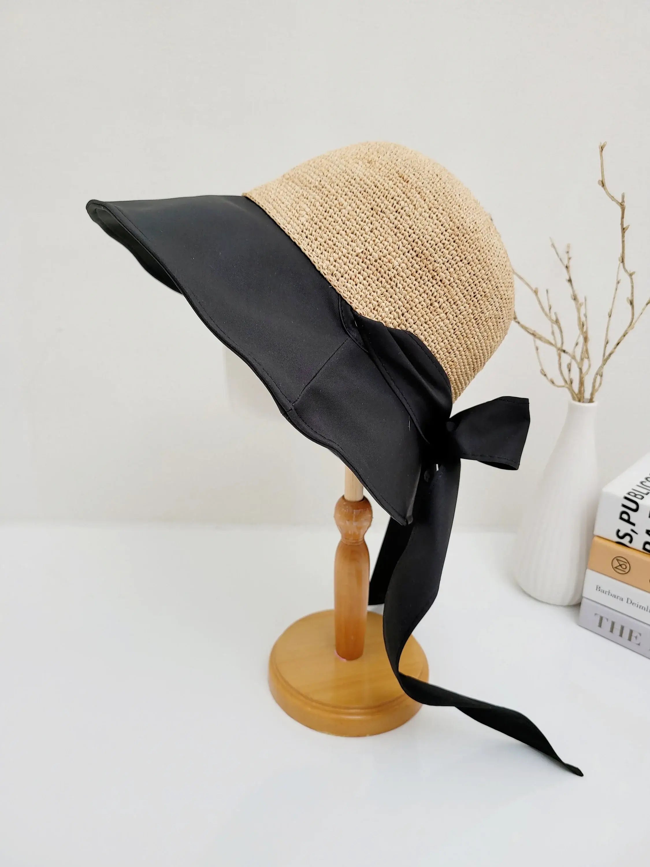 south hampton hat: Straw hat with a wide, black brim and matching black ribbon tie, displayed on a wooden stand