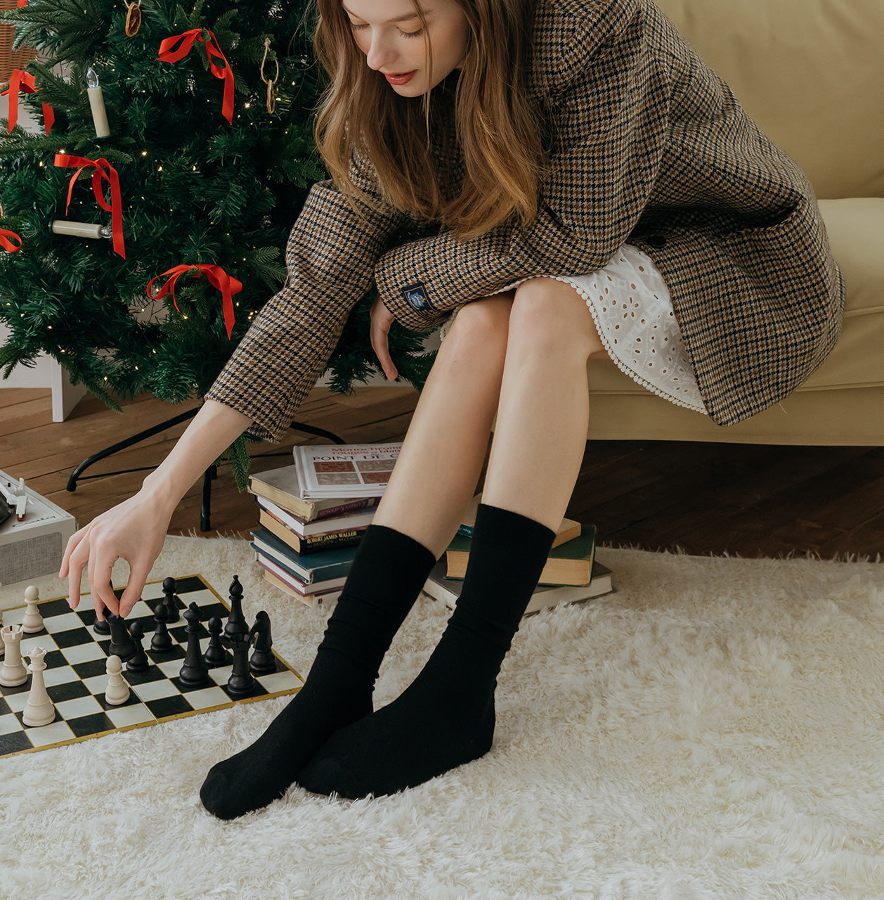 Woman playing chess in a cozy room with a Christmas tree in the background