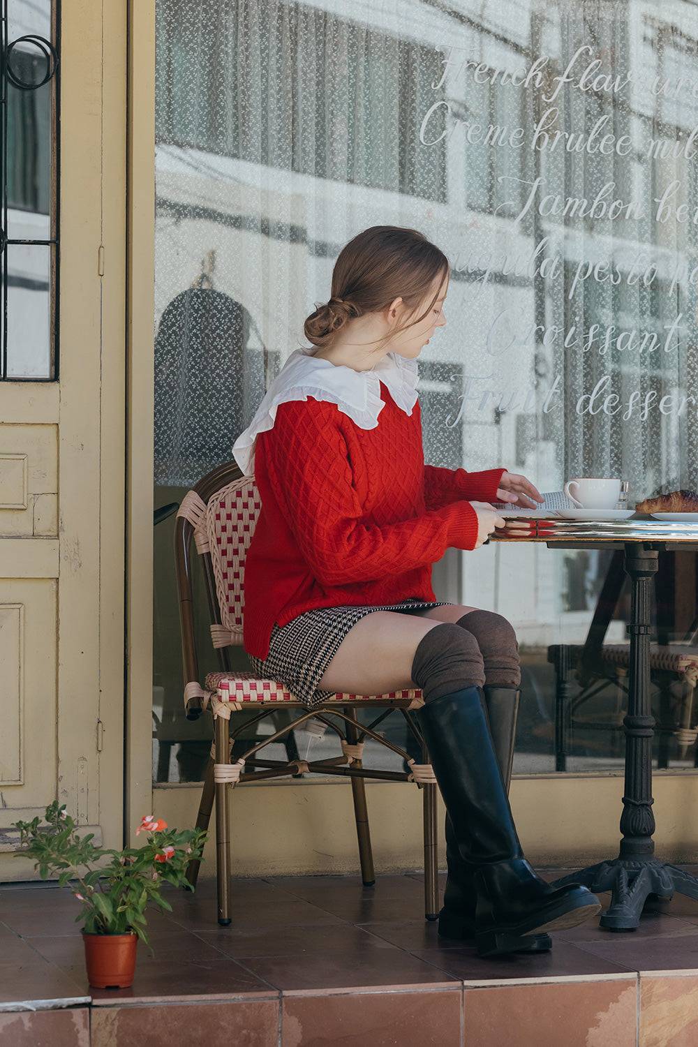 Woman in a red sweater sitting at an outdoor cafe table.