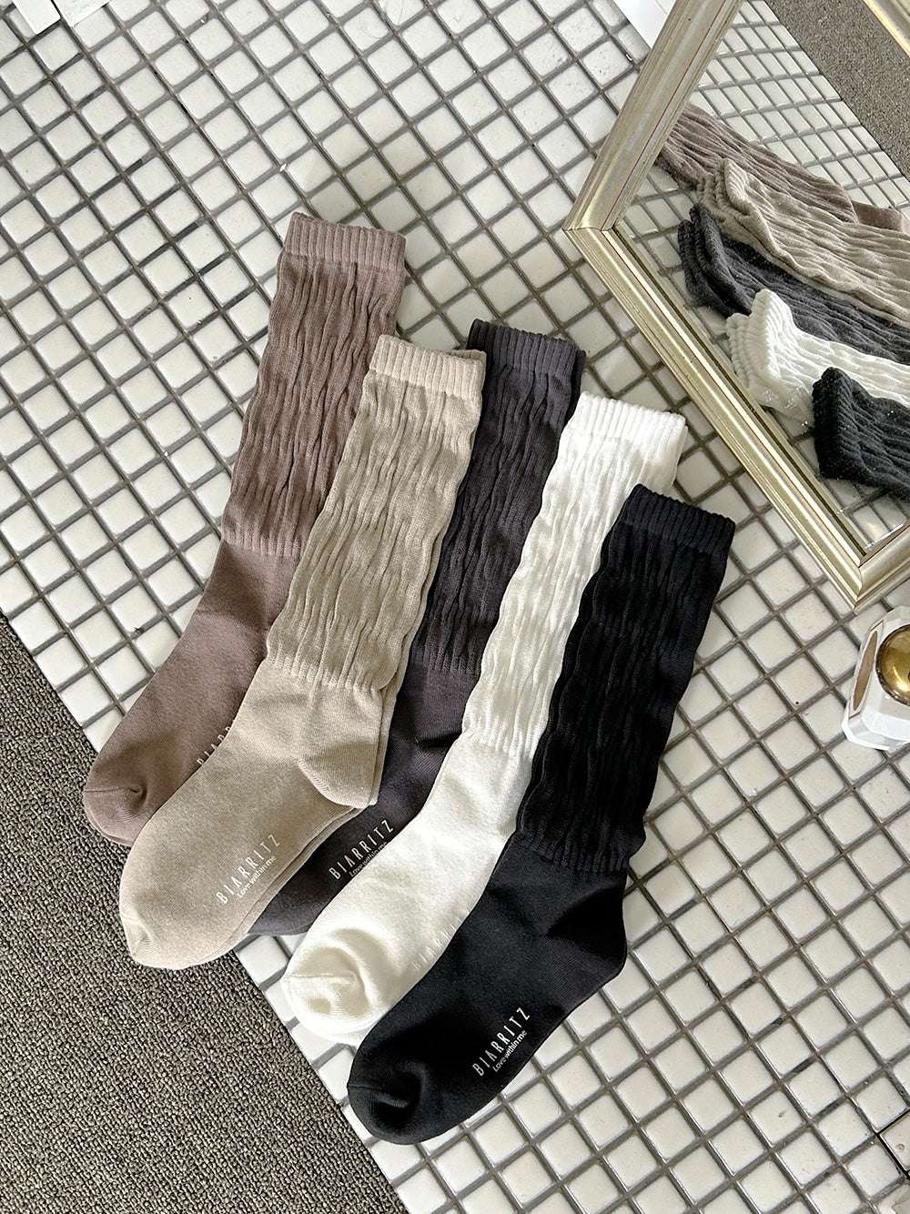 Set of four pairs of socks in brown, beige, black, and white on a checkered floor.