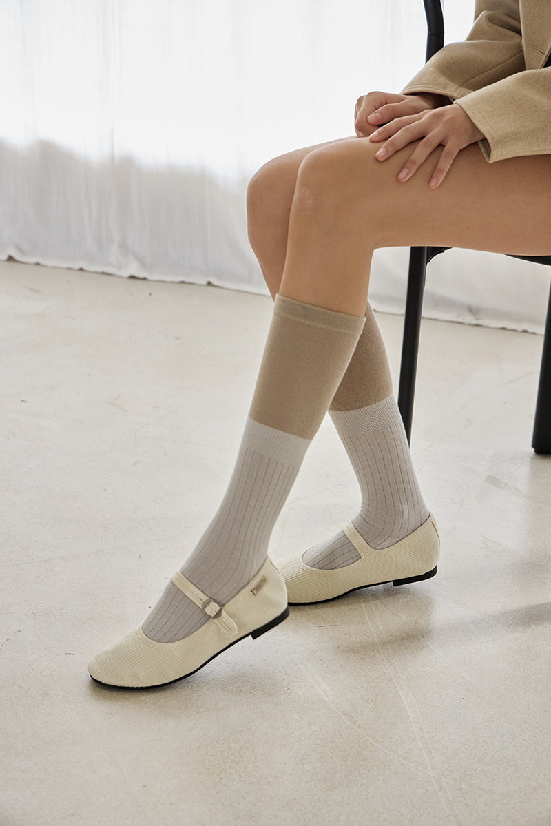 Person wearing beige knee-high socks and white shoes on a light-colored floor.