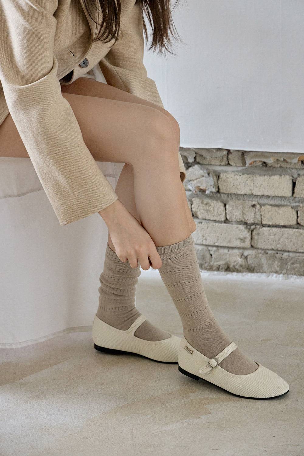 Person wearing beige shoes and socks sitting on a white surface with a stone wall background