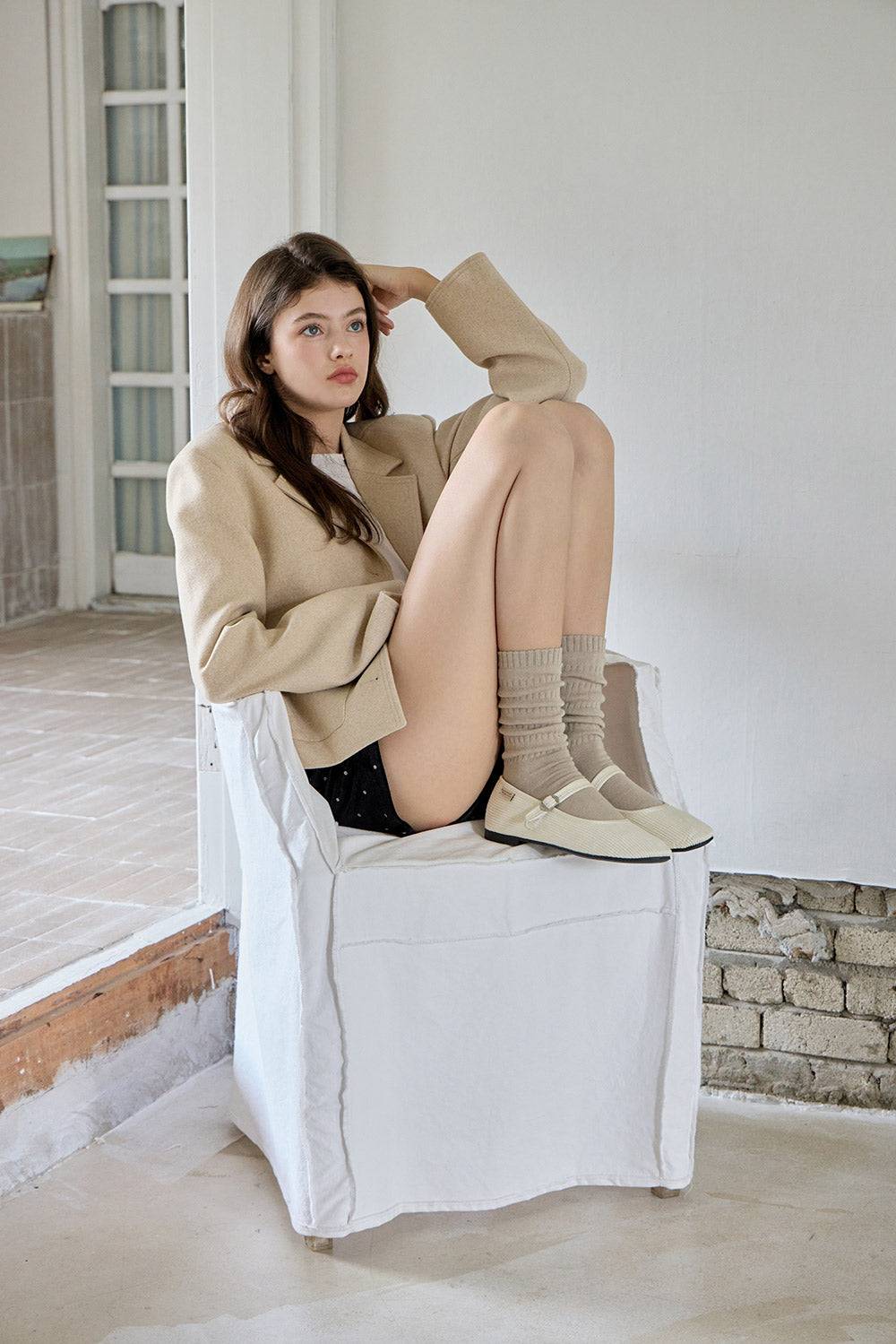Woman with beige socks sitting on a white chair in a minimalistic room.