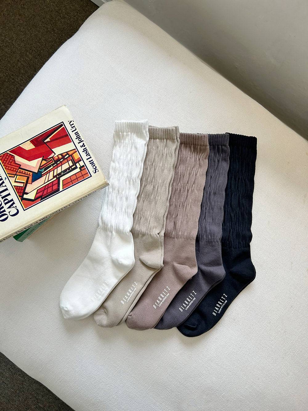 Set of five pairs of socks in white, beige, gray, and black on a white surface with a book in the background.