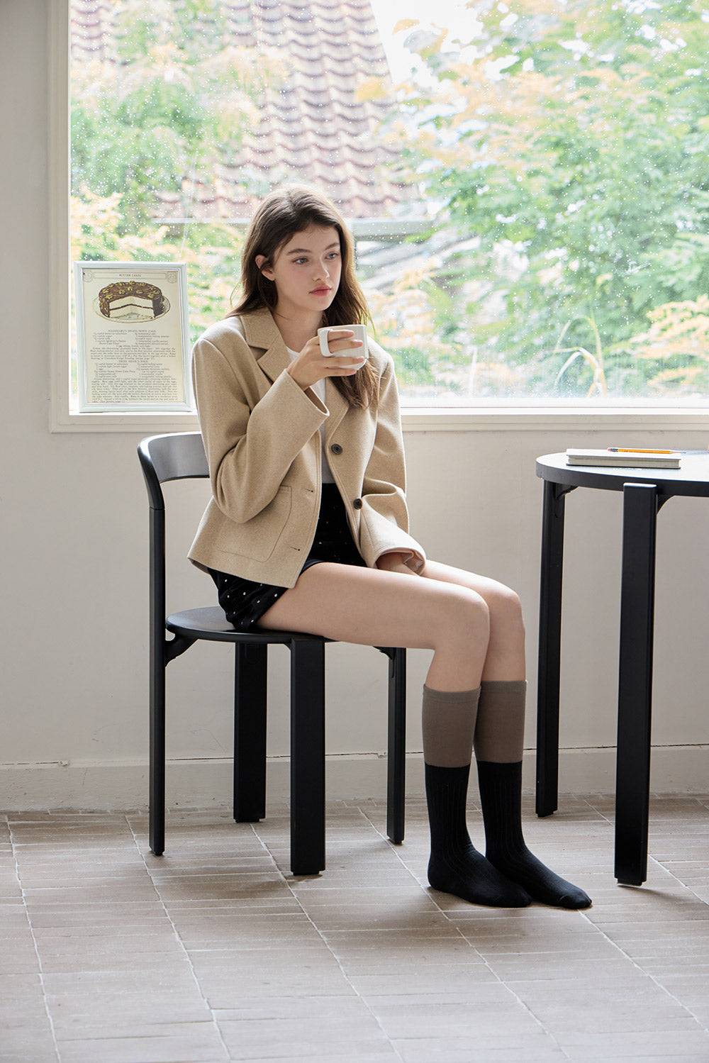 Woman sitting on a chair by a window, holding a cup.