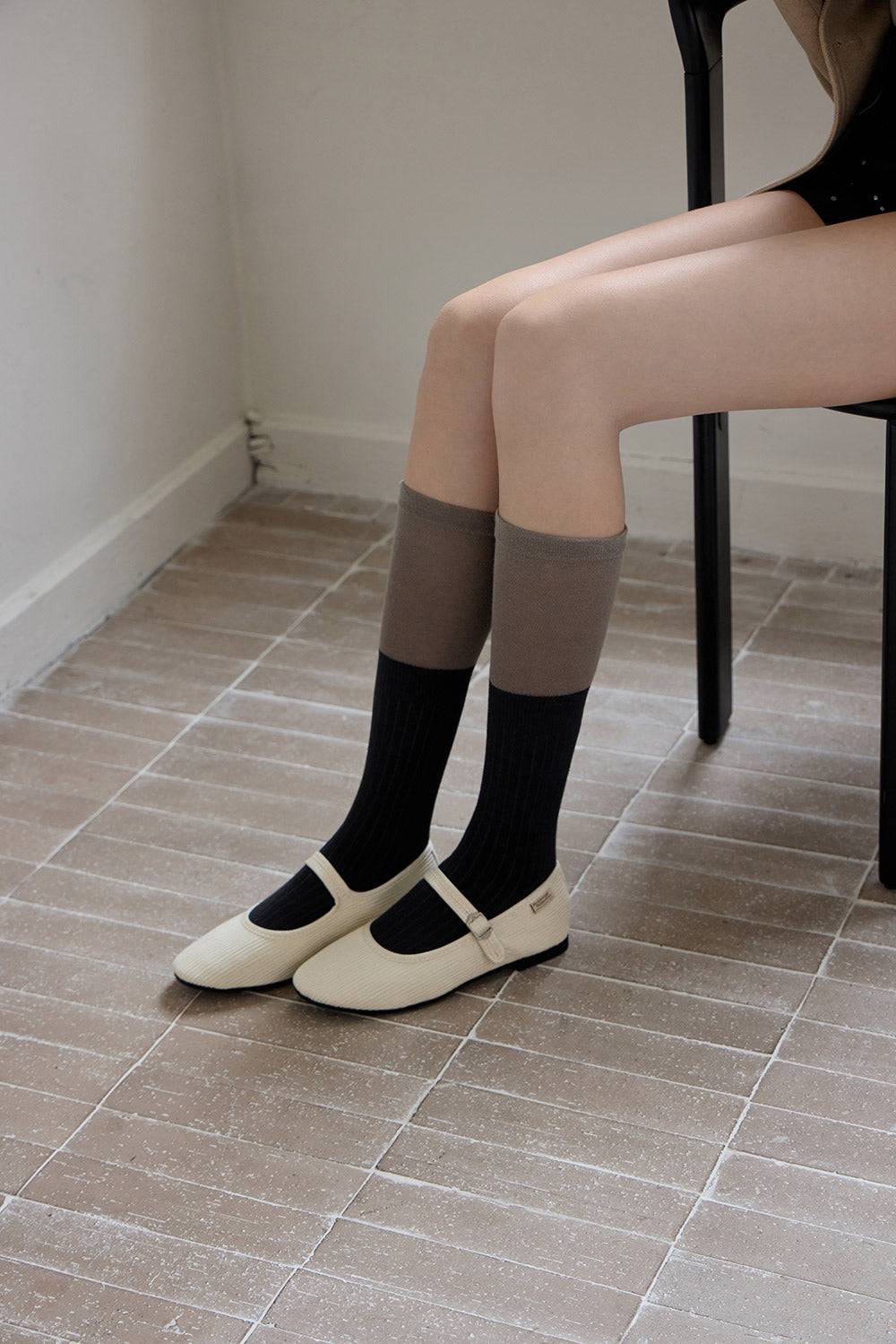 Person wearing knee-high socks and white shoes on a tiled floor.