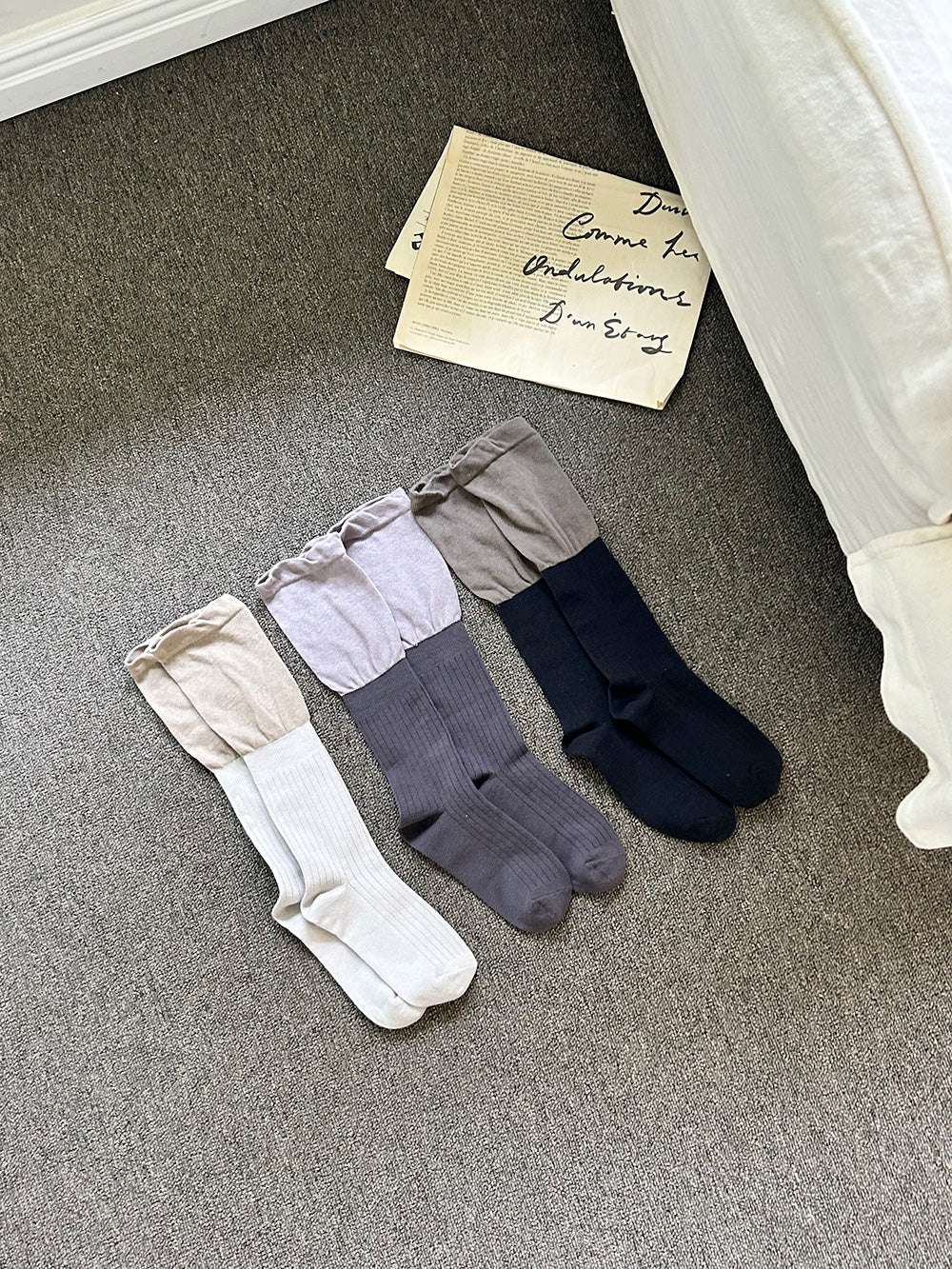 three pairs of socks in beige, gray, and navy on a carpeted floor.