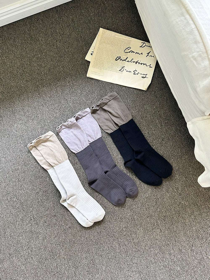 three pairs of socks in beige, gray, and navy on a carpeted floor.