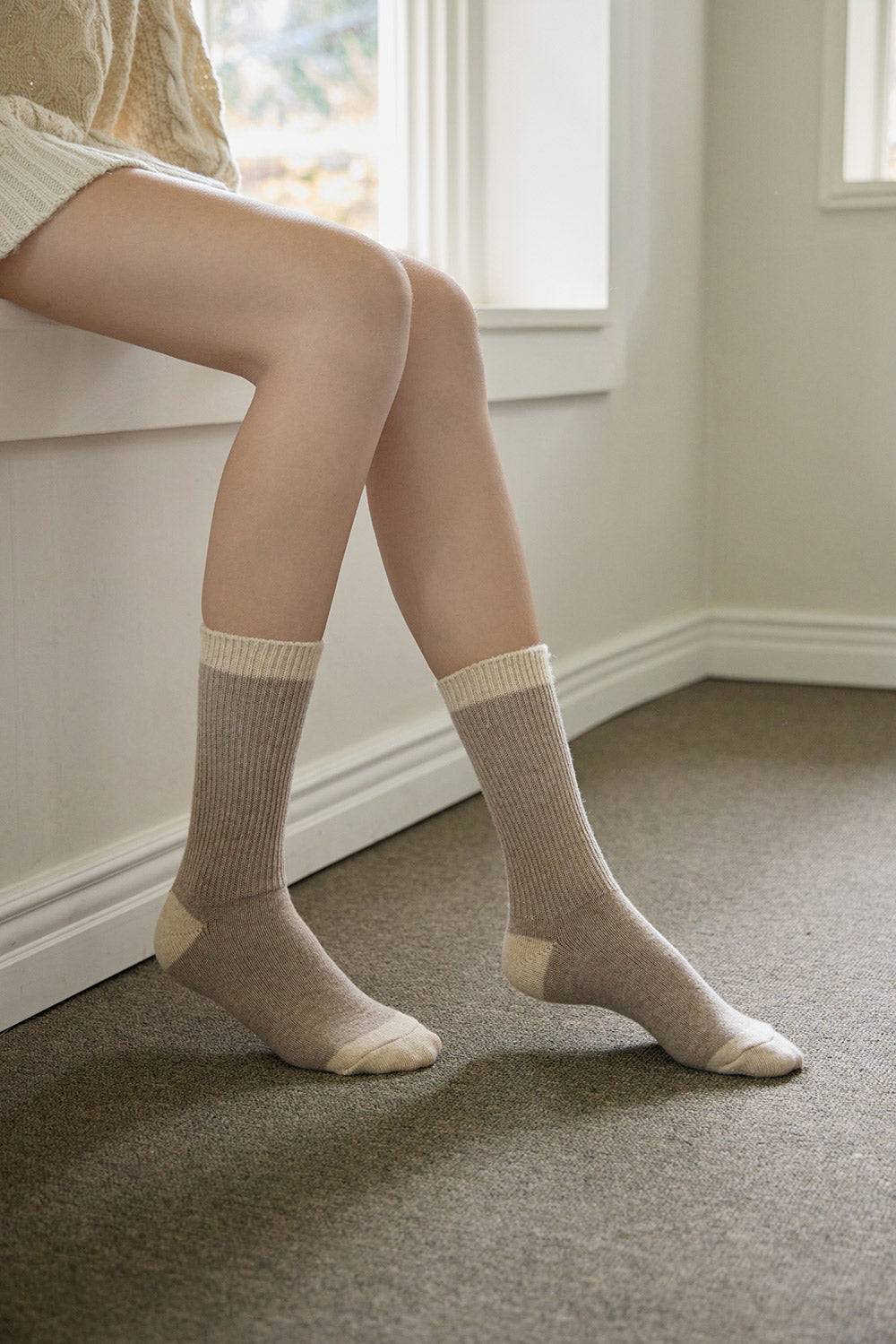 Person wearing beige socks standing on a carpeted floor with a neutral-colored wall in the background.