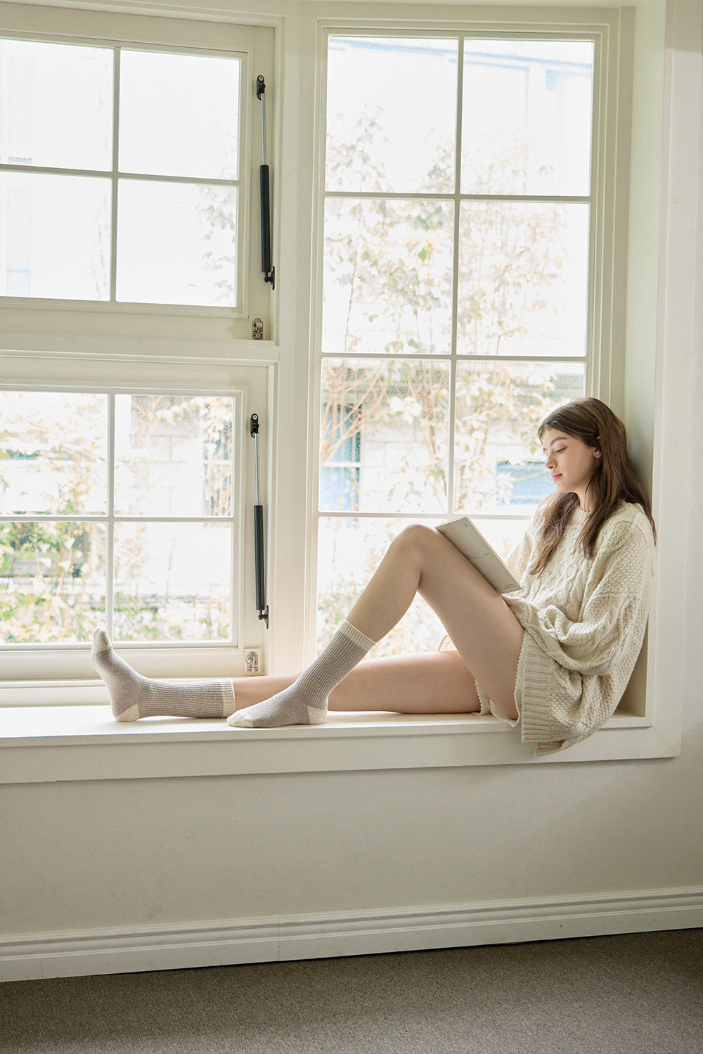 Woman sitting by a window reading a book in a bright room