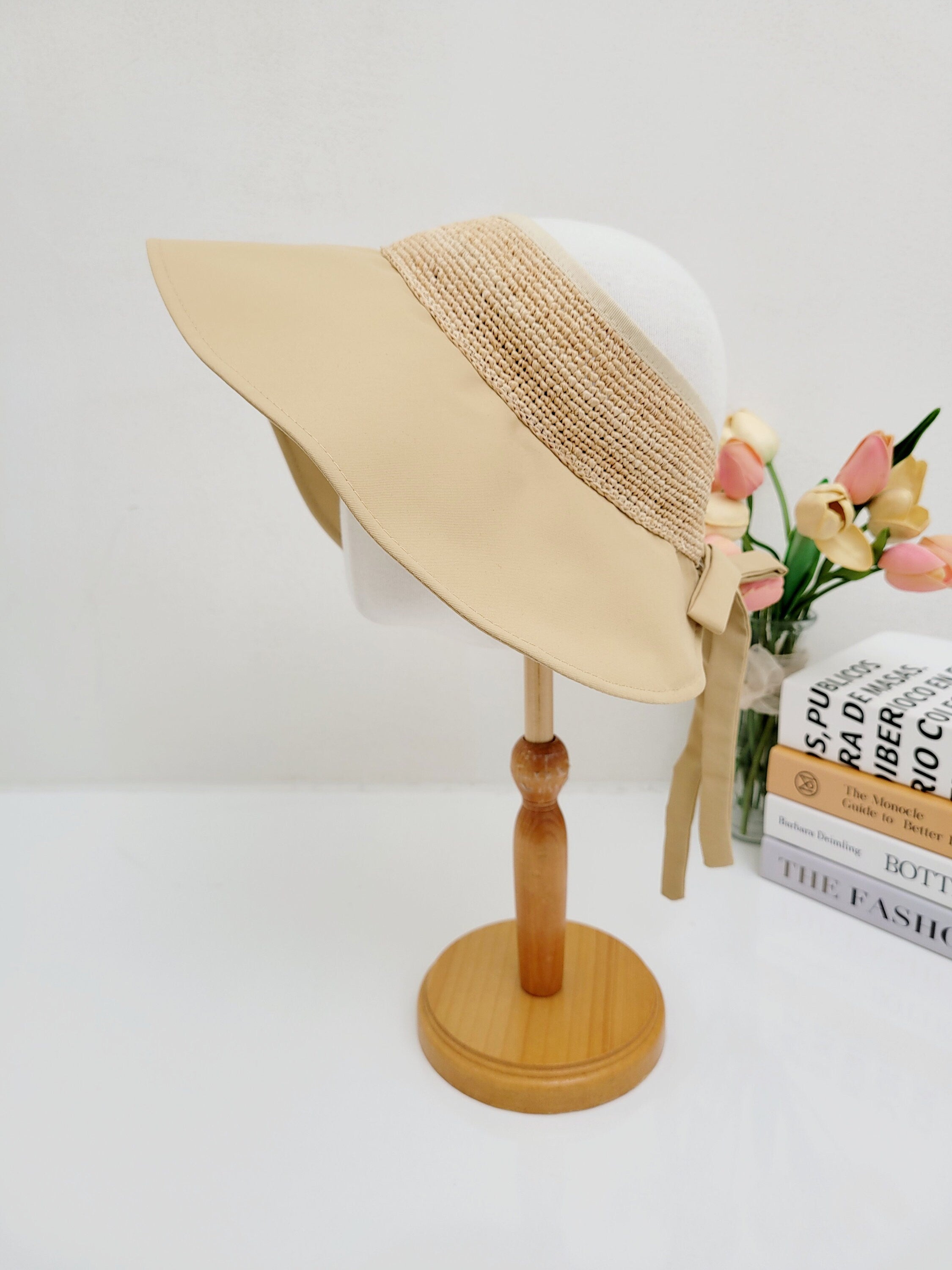 GRAYTON BEACH: Beige sun visor hat with woven band detail and tie closure, displayed on a wooden stand