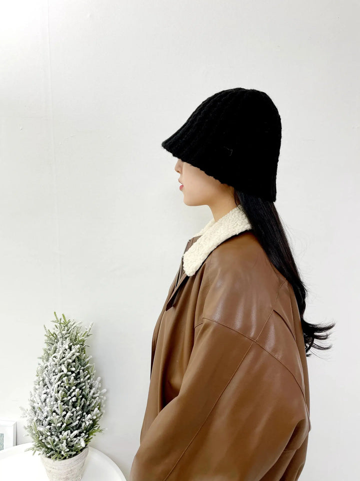 Woman in brown leather jacket and black "beanie the wool-vol3". The knitted beanie covers her forehead, standing near a mini Christmas tree.