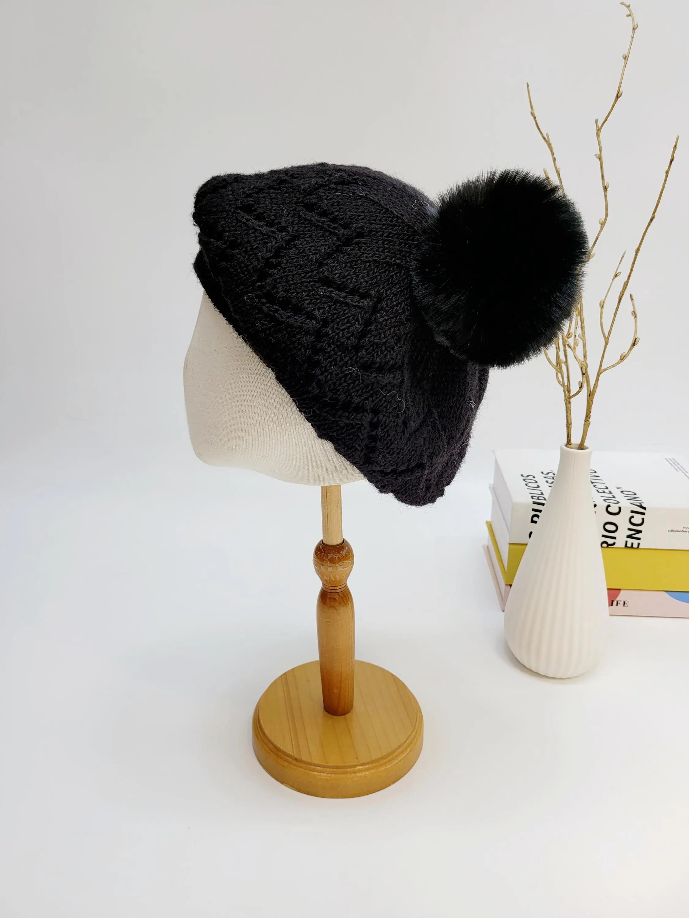 Black knit emma in paris beanie with a large faux fur pompom. Features a subtle cable knit pattern, perfect for winter.