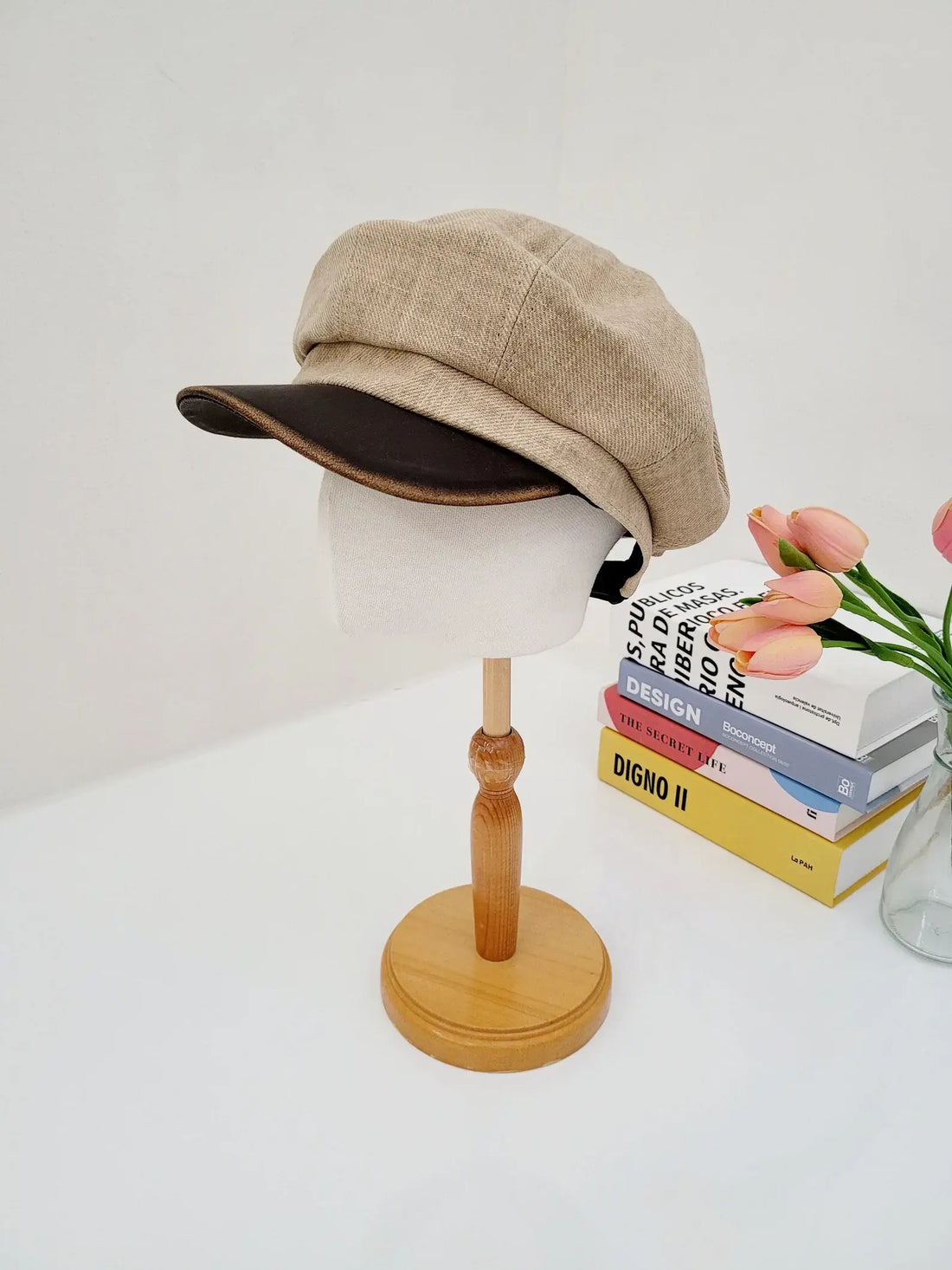Beige lana beret on a wooden stand. A stylish baker boy hat with a dark brown brim.