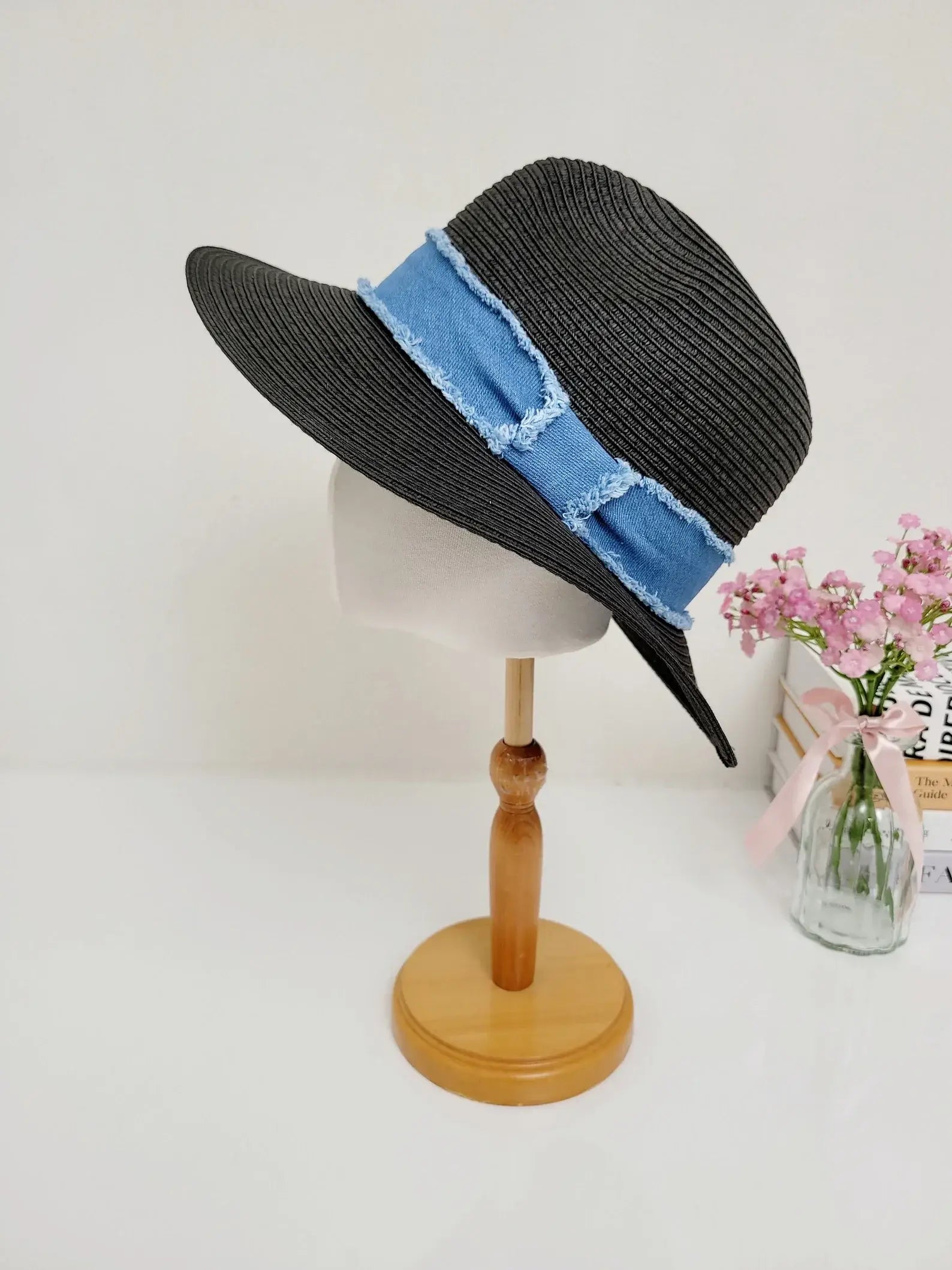 long island black straw sun hat with a frayed blue denim band, displayed on a wooden stand with flowers, providing stylish sun protection
