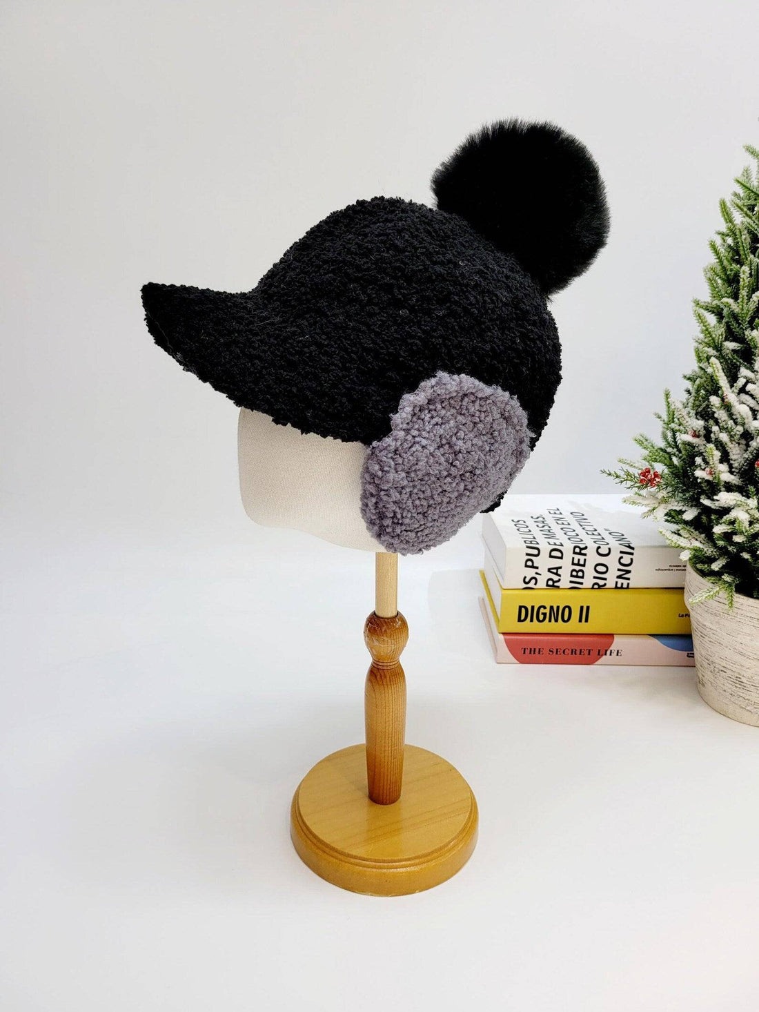 Black textured woof woof hat with gray ear flaps and a fluffy pom-pom, displayed on a mannequin head.