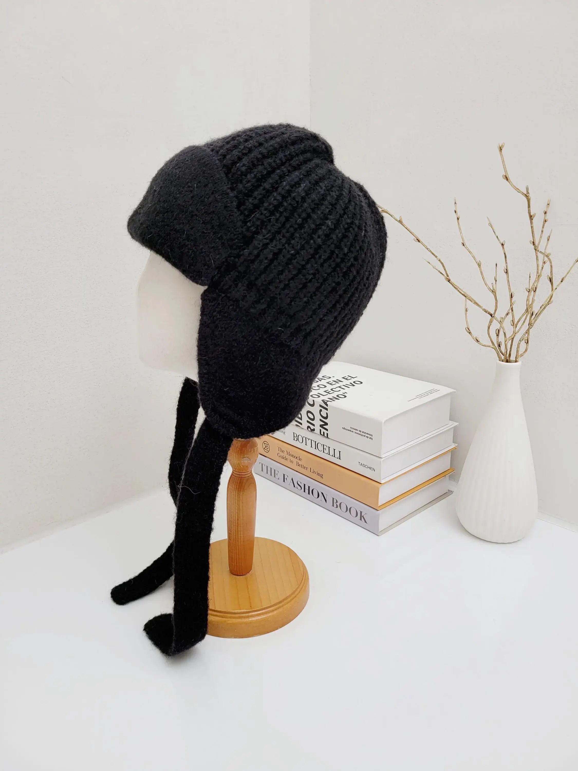 A black knitted winter hat with ear flap, made of alpaca, wool, and nylon, displayed on a mannequin head.