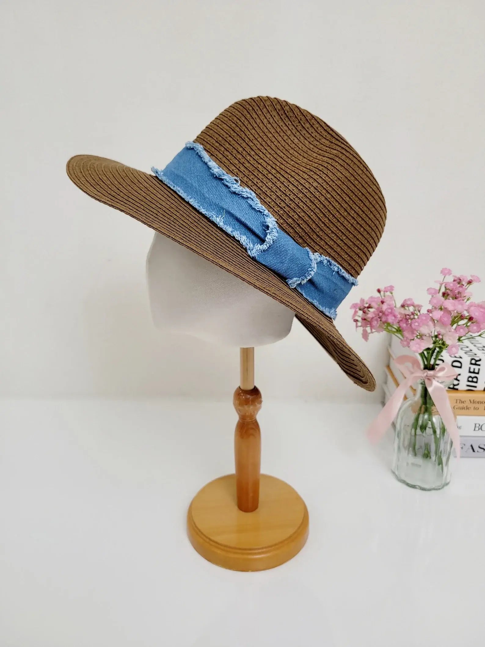 long island: Brown woven straw sun hat with a stylish frayed denim band, displayed on a wooden stand.