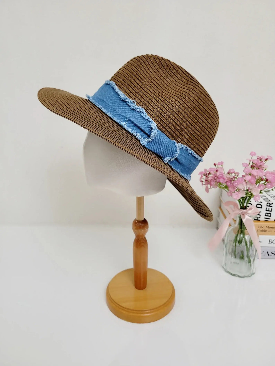 long island: Brown woven straw sun hat with a stylish frayed denim band, displayed on a wooden stand.