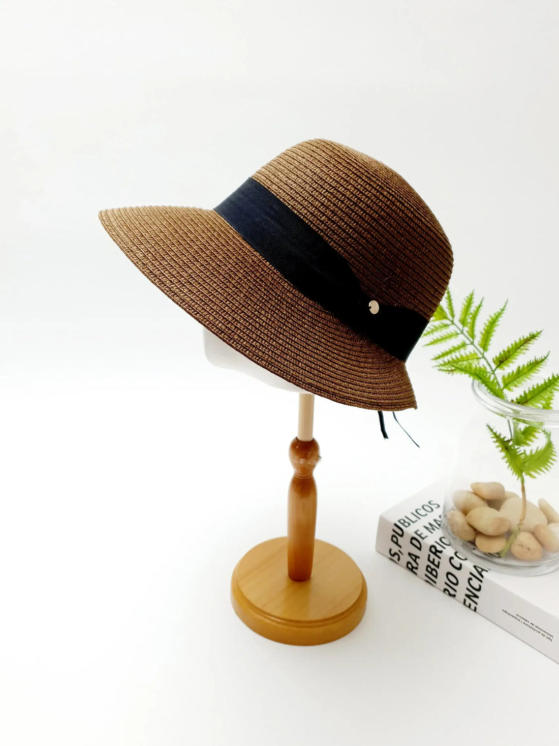 Brown woven isabelle sun hat with a stylish black band and a small metallic accent, displayed on a wooden stand.