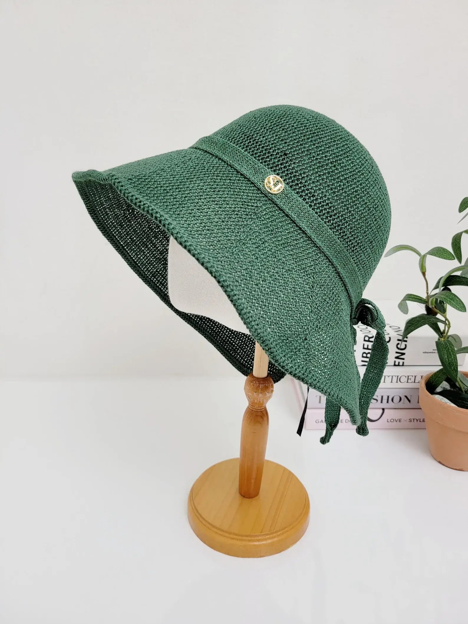 Green woven sun hat with a stylish ribbon tie and decorative button detail, offering sun protection and a fashionable look.