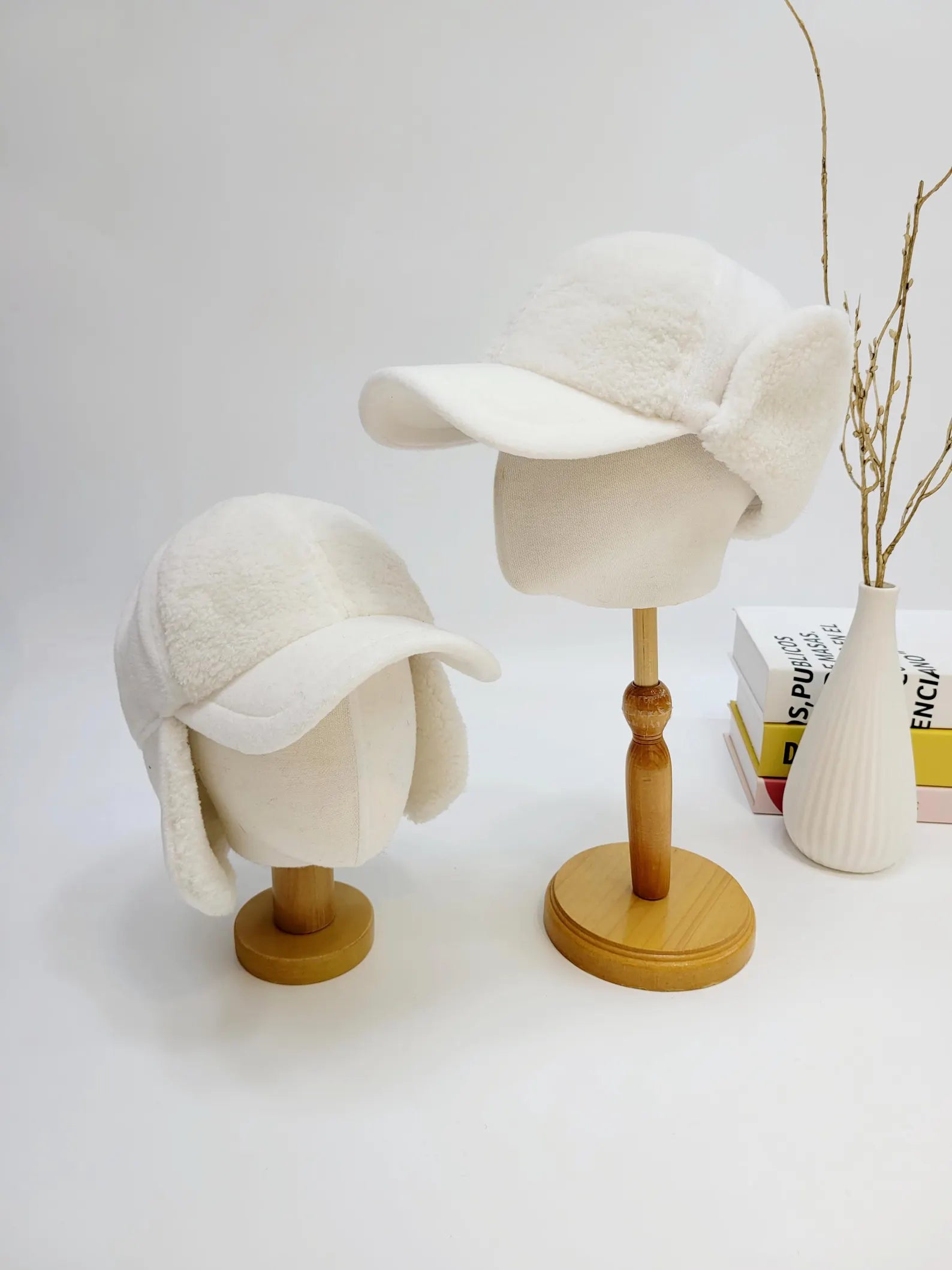 Two white jennifer on the street - winter hats, one slightly smaller, both featuring faux fur, ear flaps and a short brim, displayed on mannequin heads.