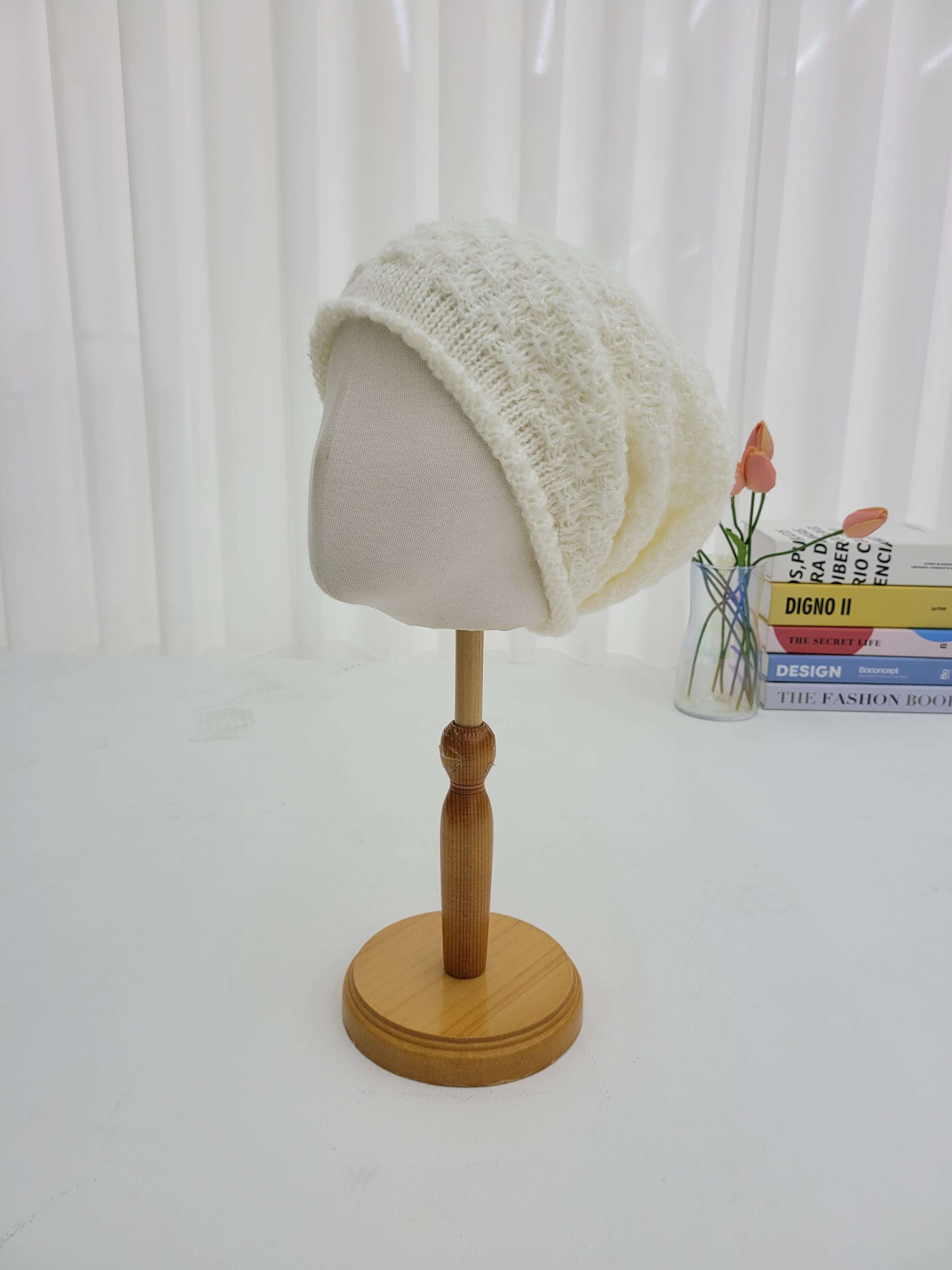 White knit cap on a wooden wall hook against a white background