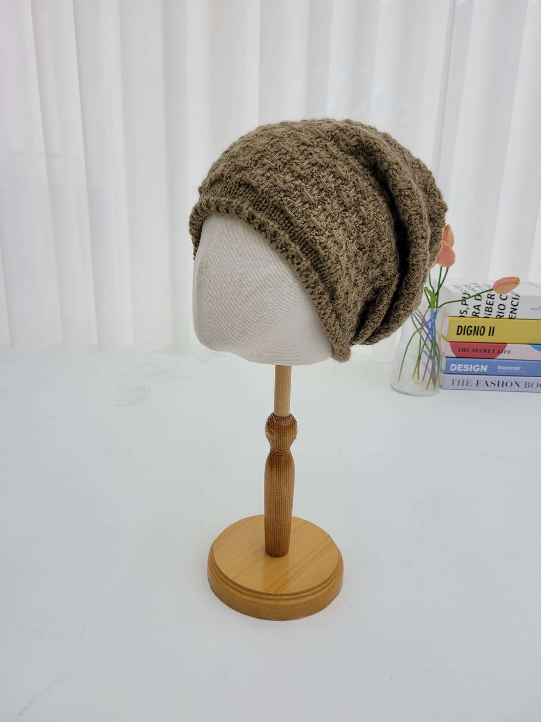 Knitted brown beanie on a mannequin head with a wooden stand against a white background