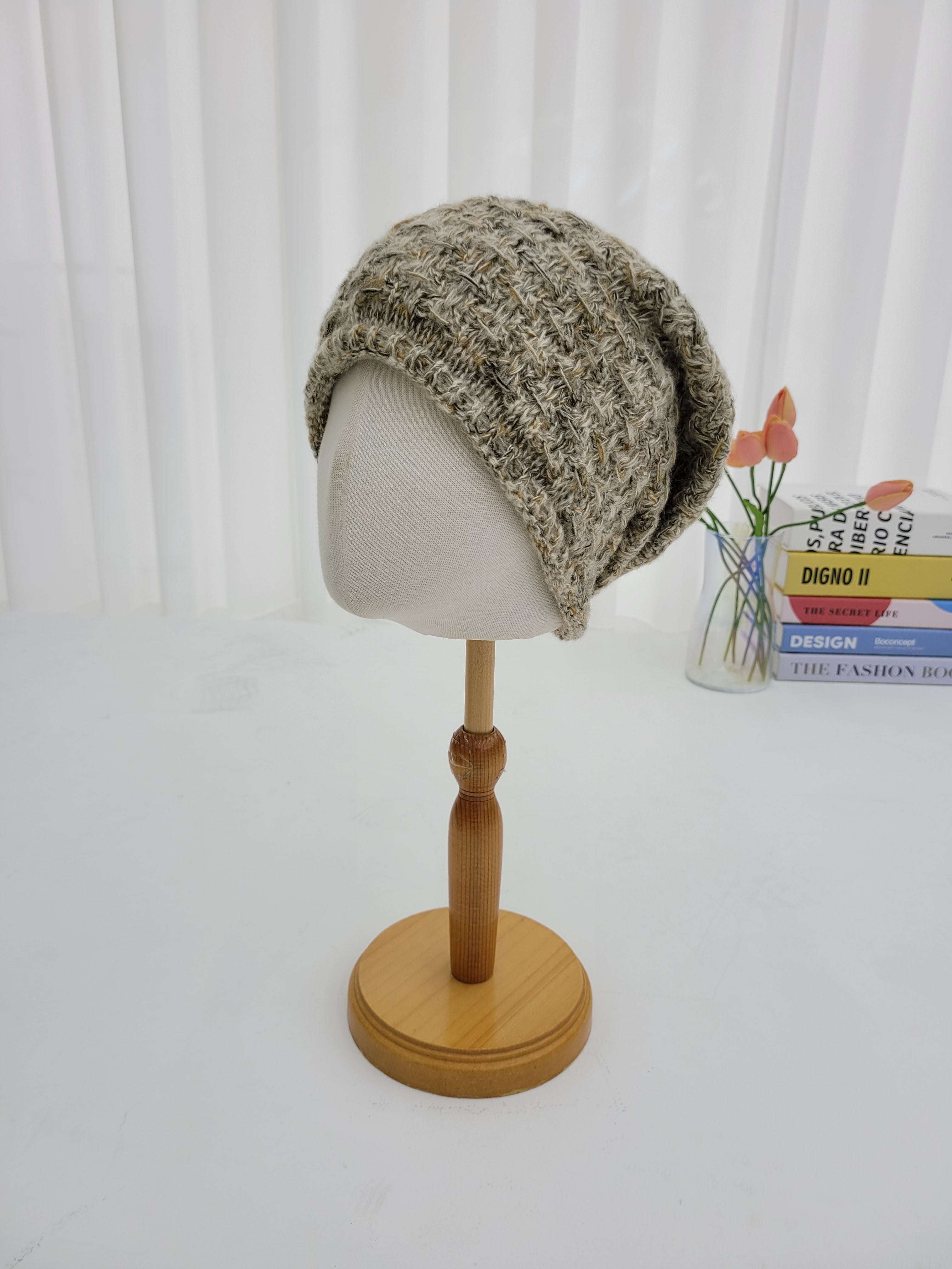 Knitted beanie on a mannequin head with a wooden stand against a white background