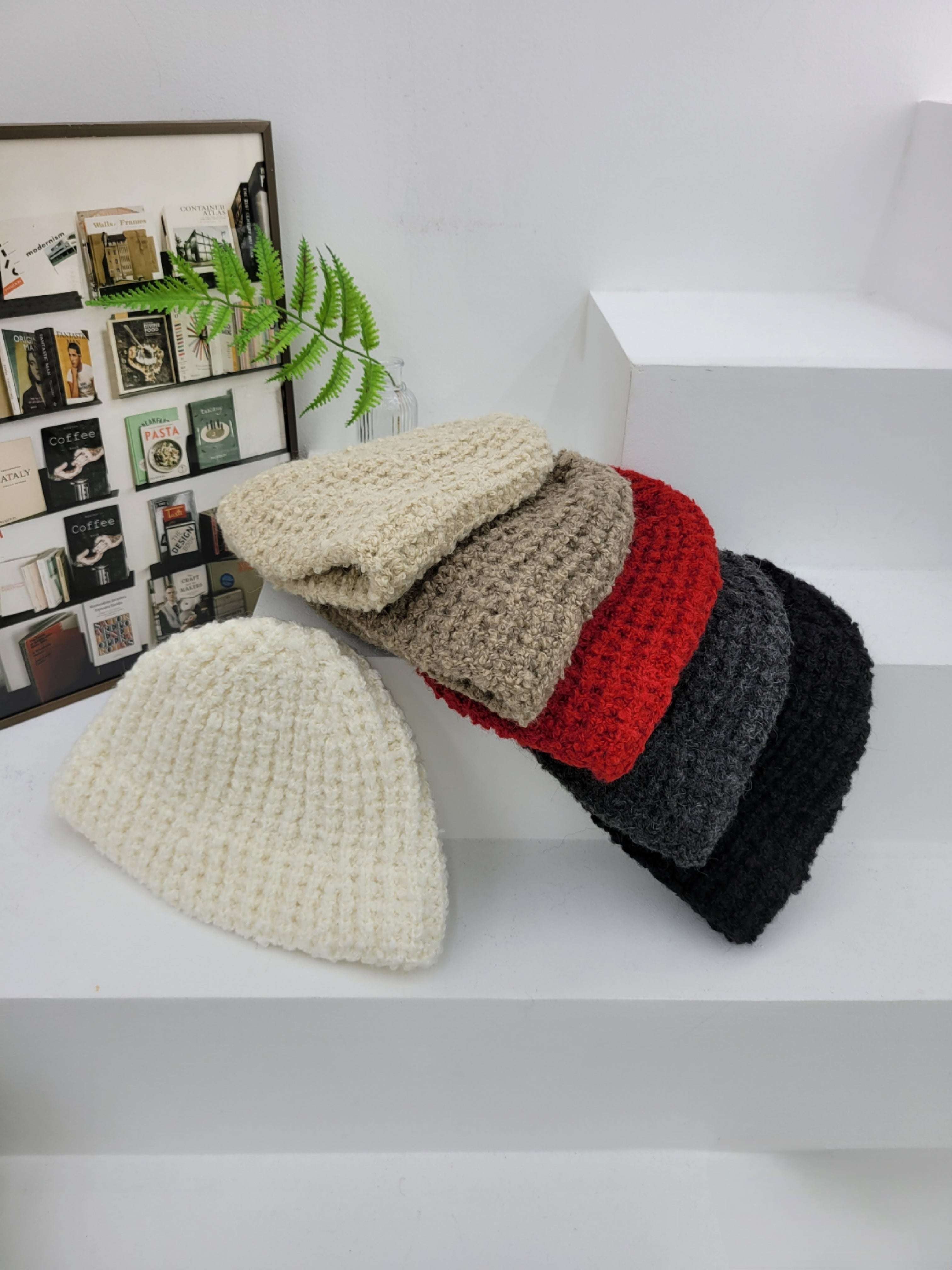 Stack of knitted beanies in various colors on a white surface with a decorative background.