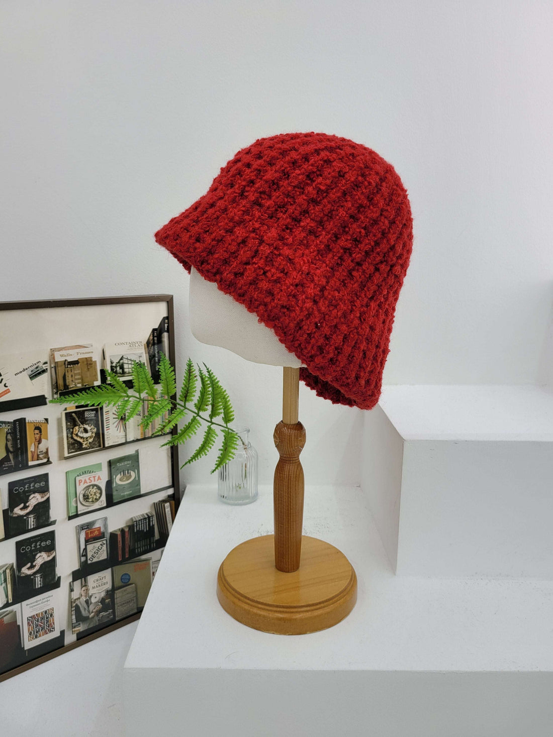 Red knitted hat on a white shelf with a wooden handle and decorative items below.