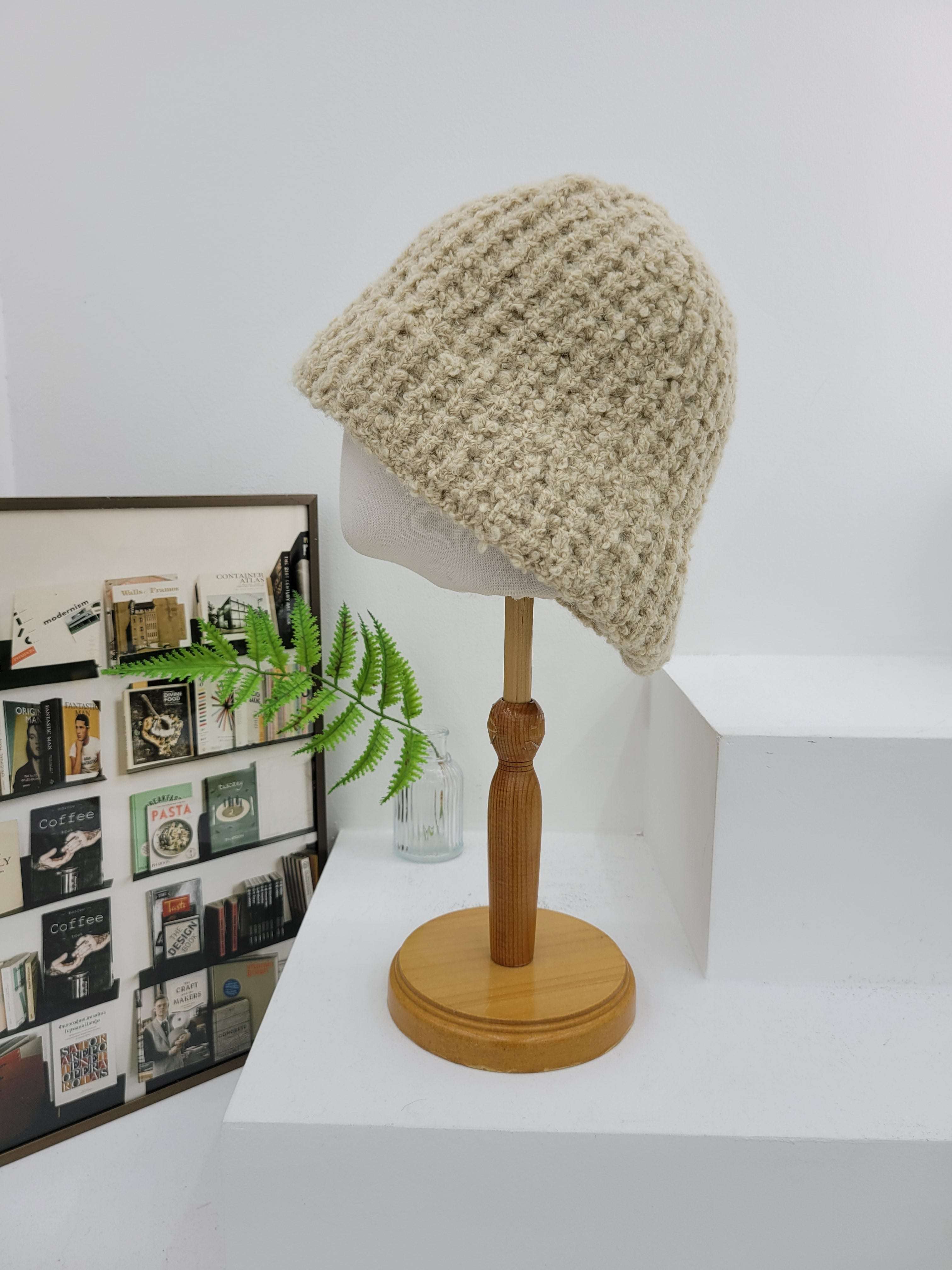 Beige knitted beanie on a white wall-mounted lamp with a wooden arm, next to a framed photo collage.