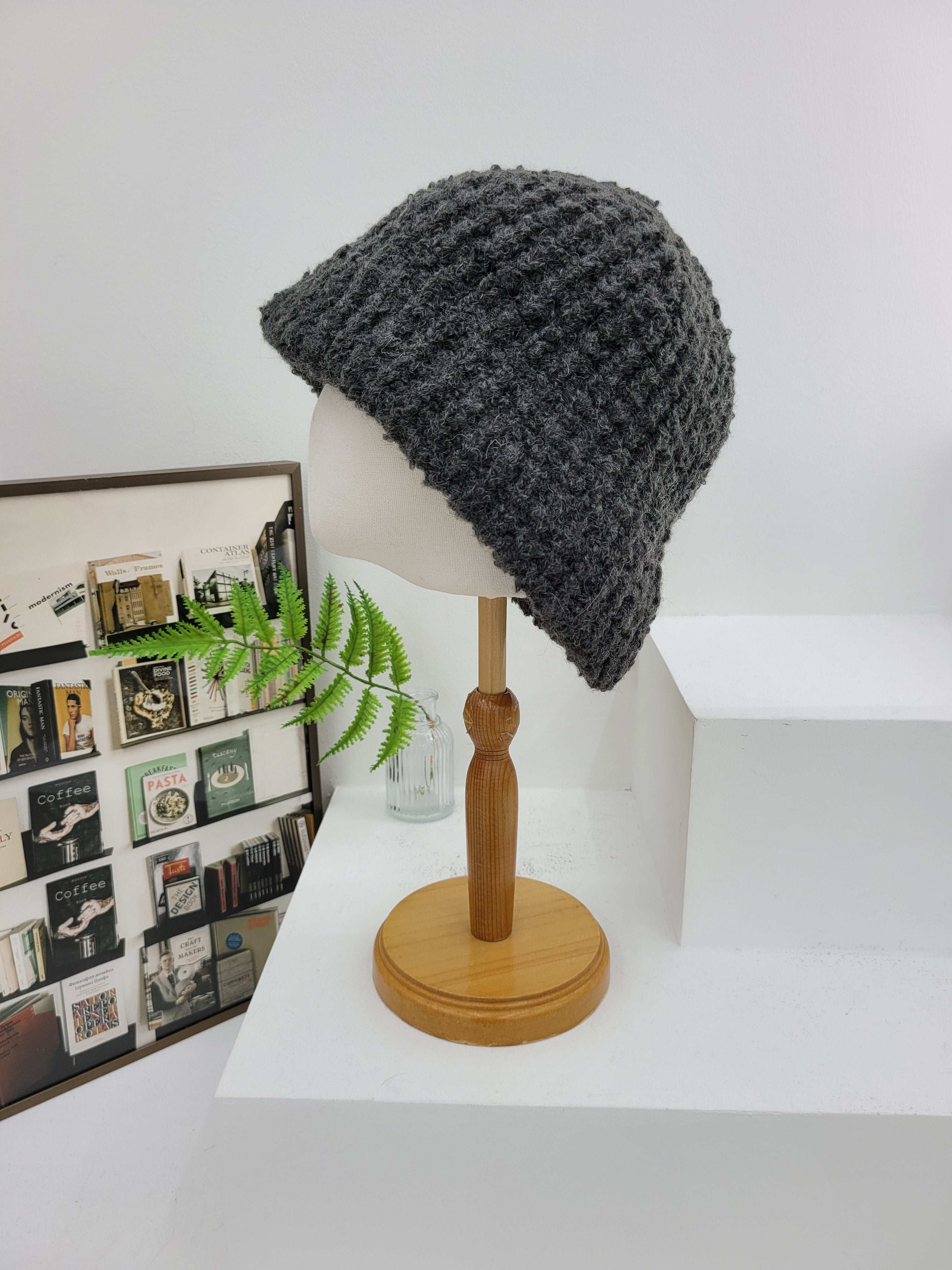 Gray knit beanie on a mannequin head against a white wall with a wooden lamp and framed photos in the background.