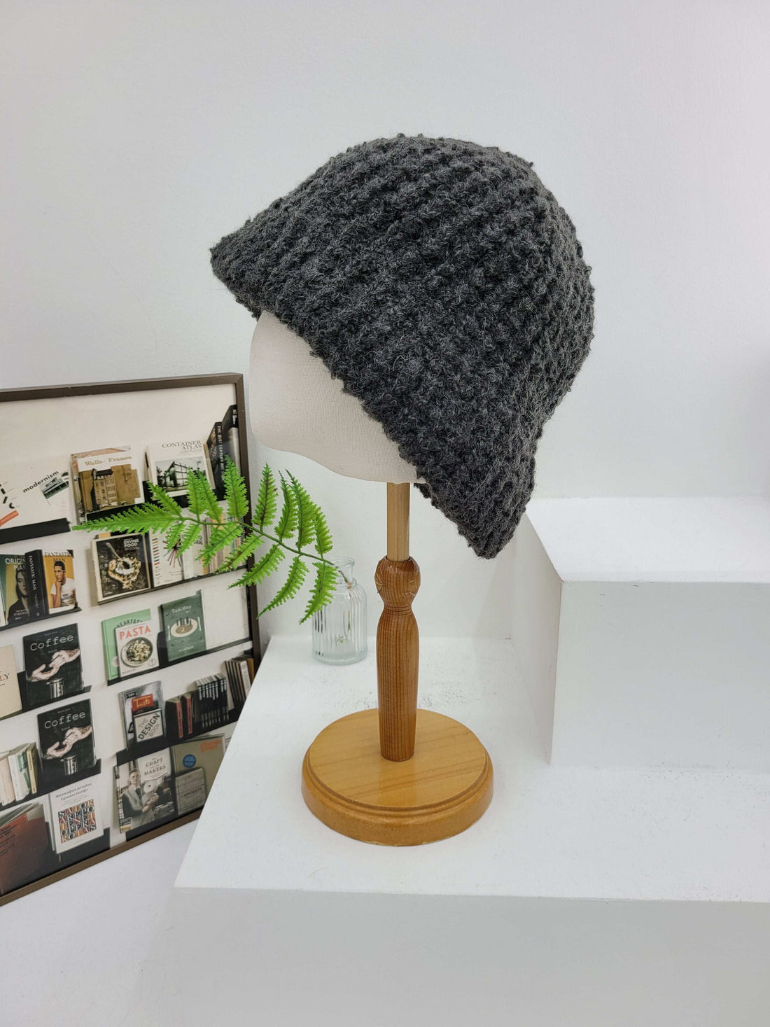 Gray knit beanie on a mannequin head against a white wall with a wooden lamp and framed photos in the background.