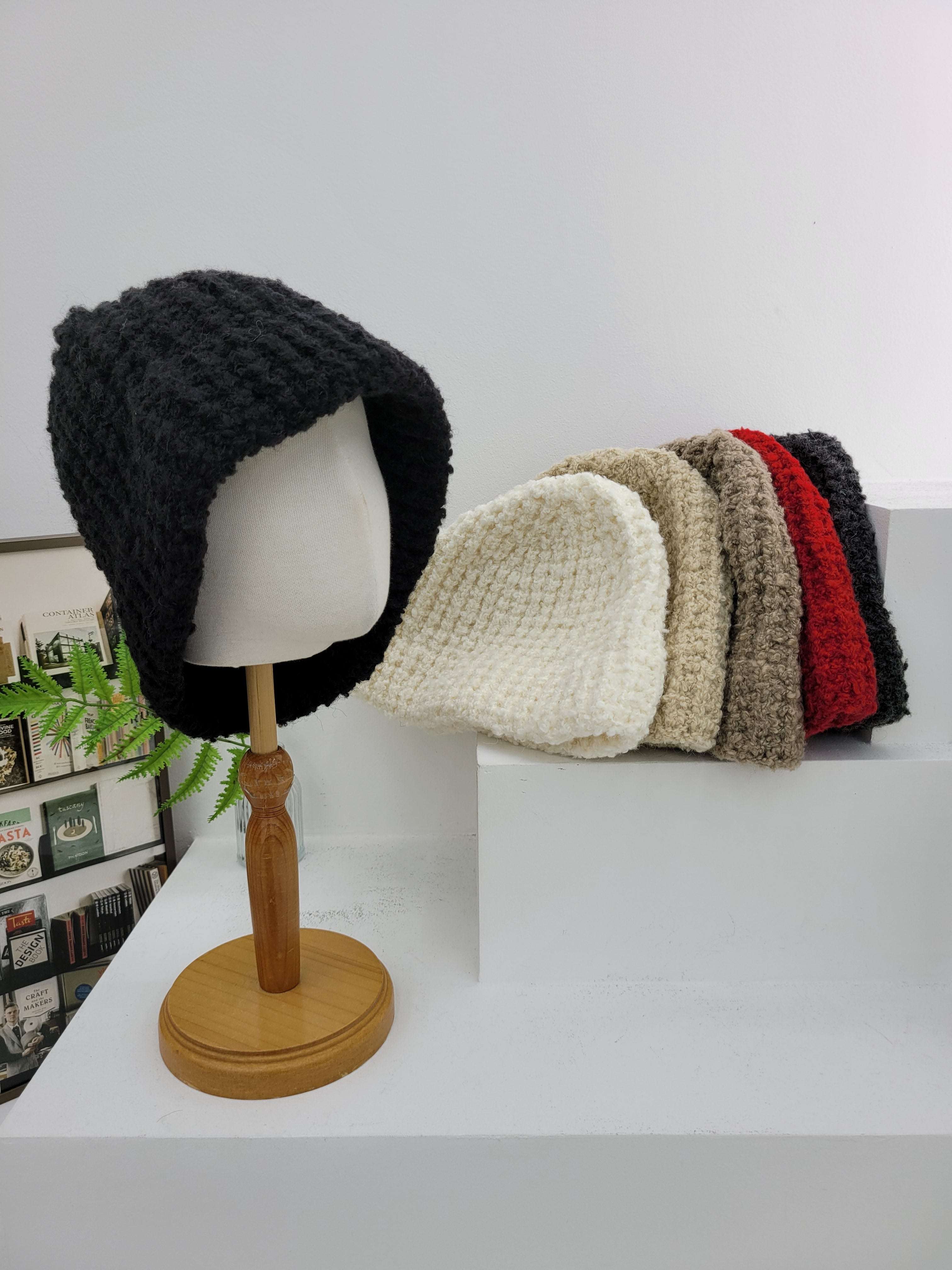Stack of knitted beanies on a wooden hook against a white wall.