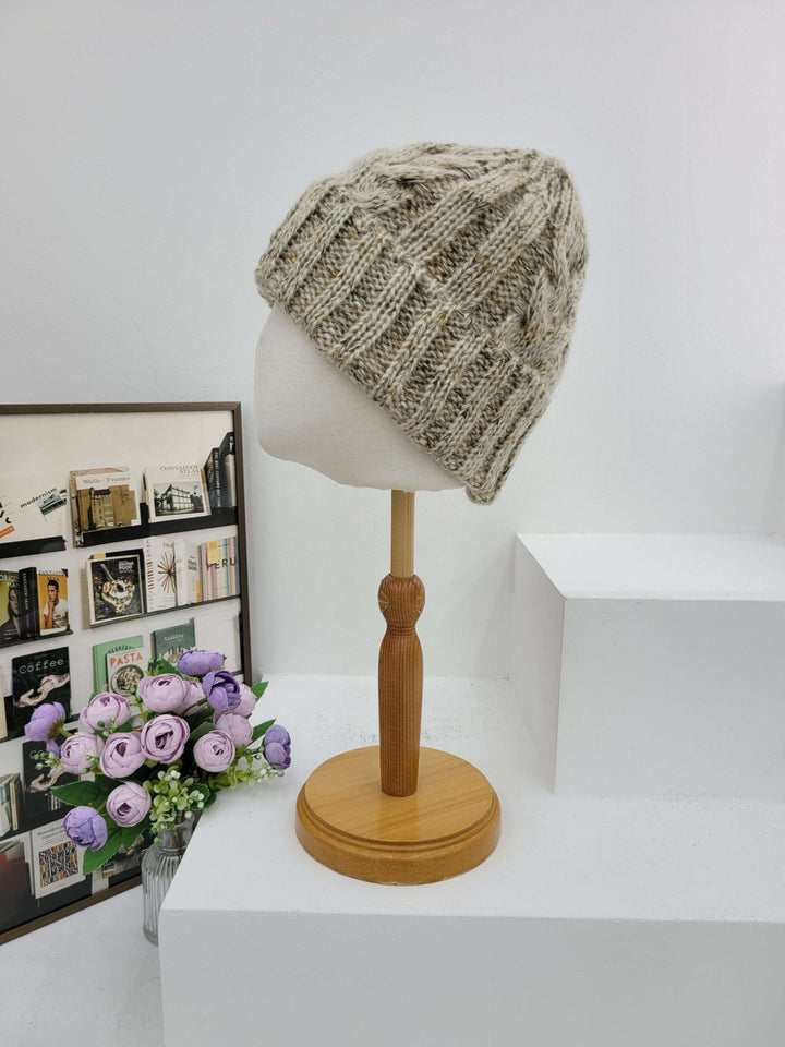 Knitted beanie on a mannequin head with a wooden lamp and flowers in the background