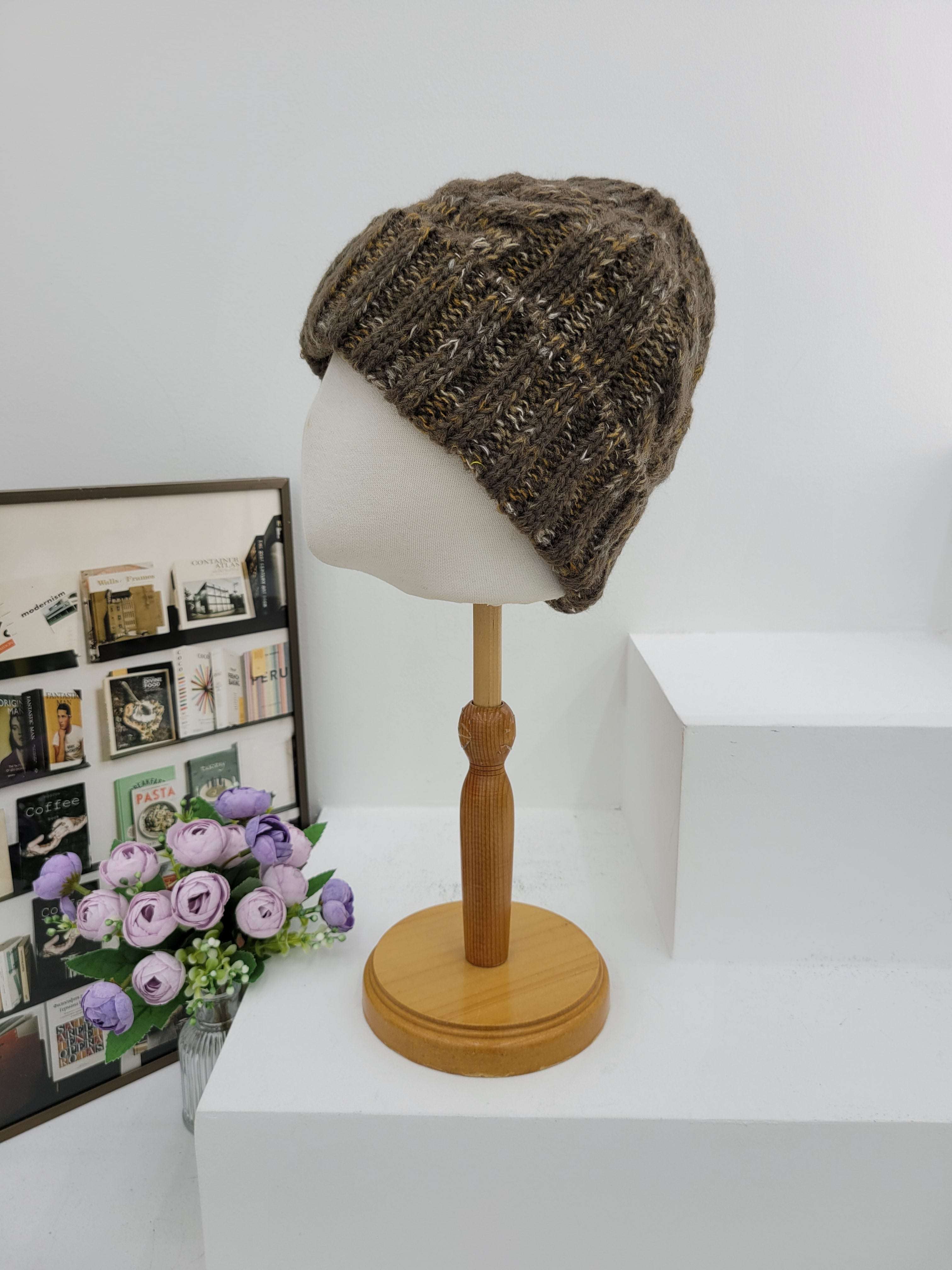 Knitted beanie on a lampshade with a wooden arm, next to a box of stamps and a bouquet of flowers.