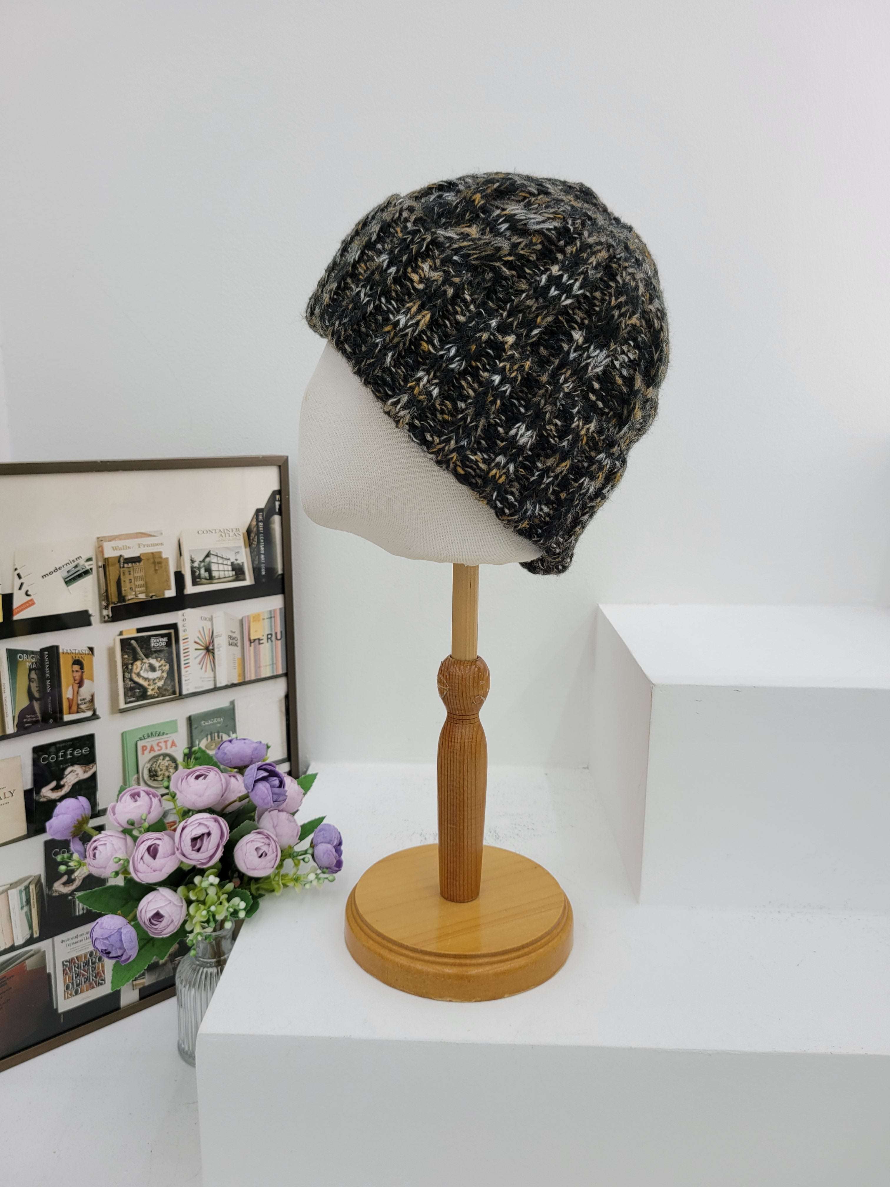 Textured beanie on a lampshade with a wooden base, next to a small bouquet of flowers on a surface.
