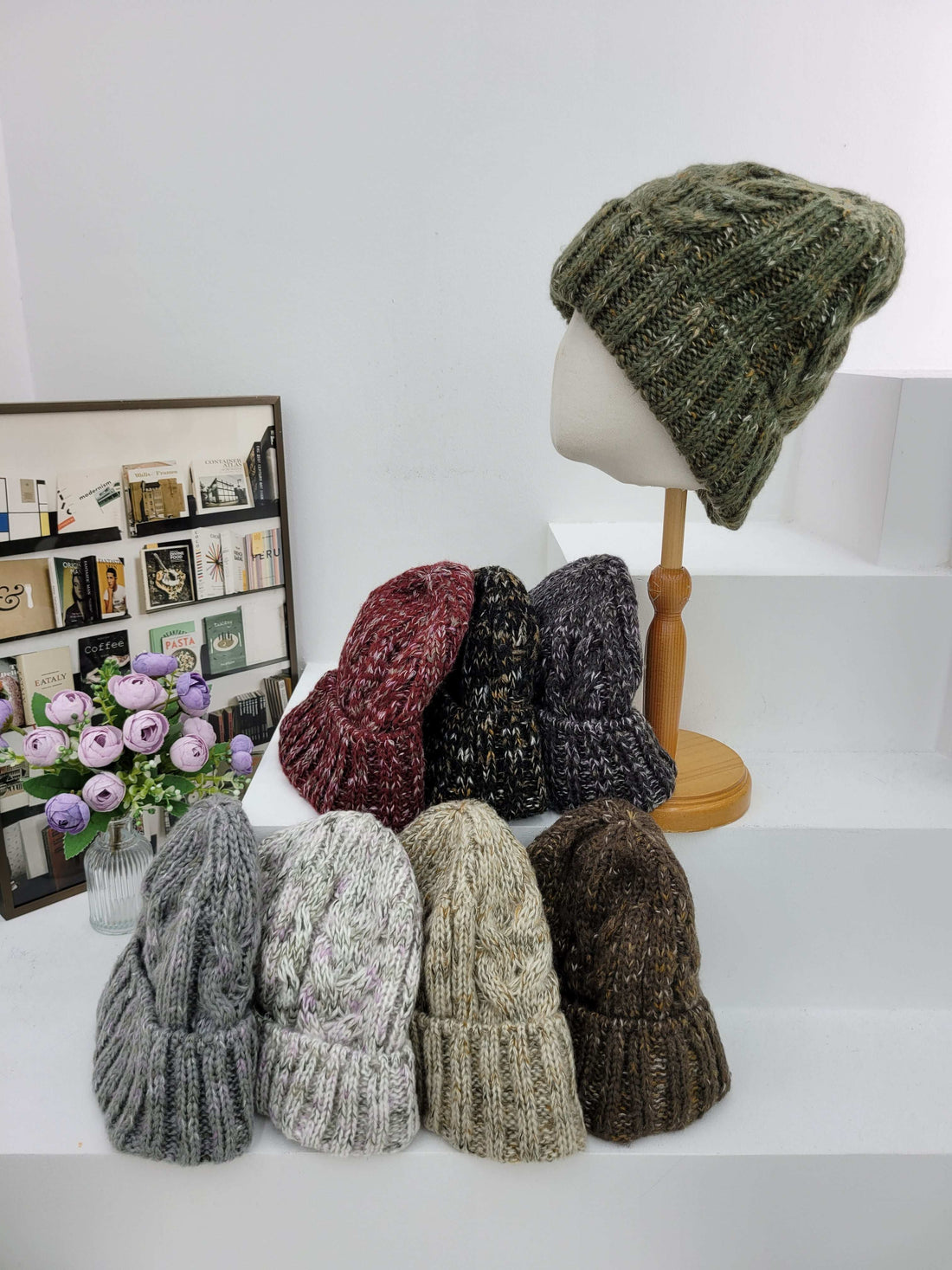 Collection of knitted hats displayed on a mannequin and wooden rack against a white background.