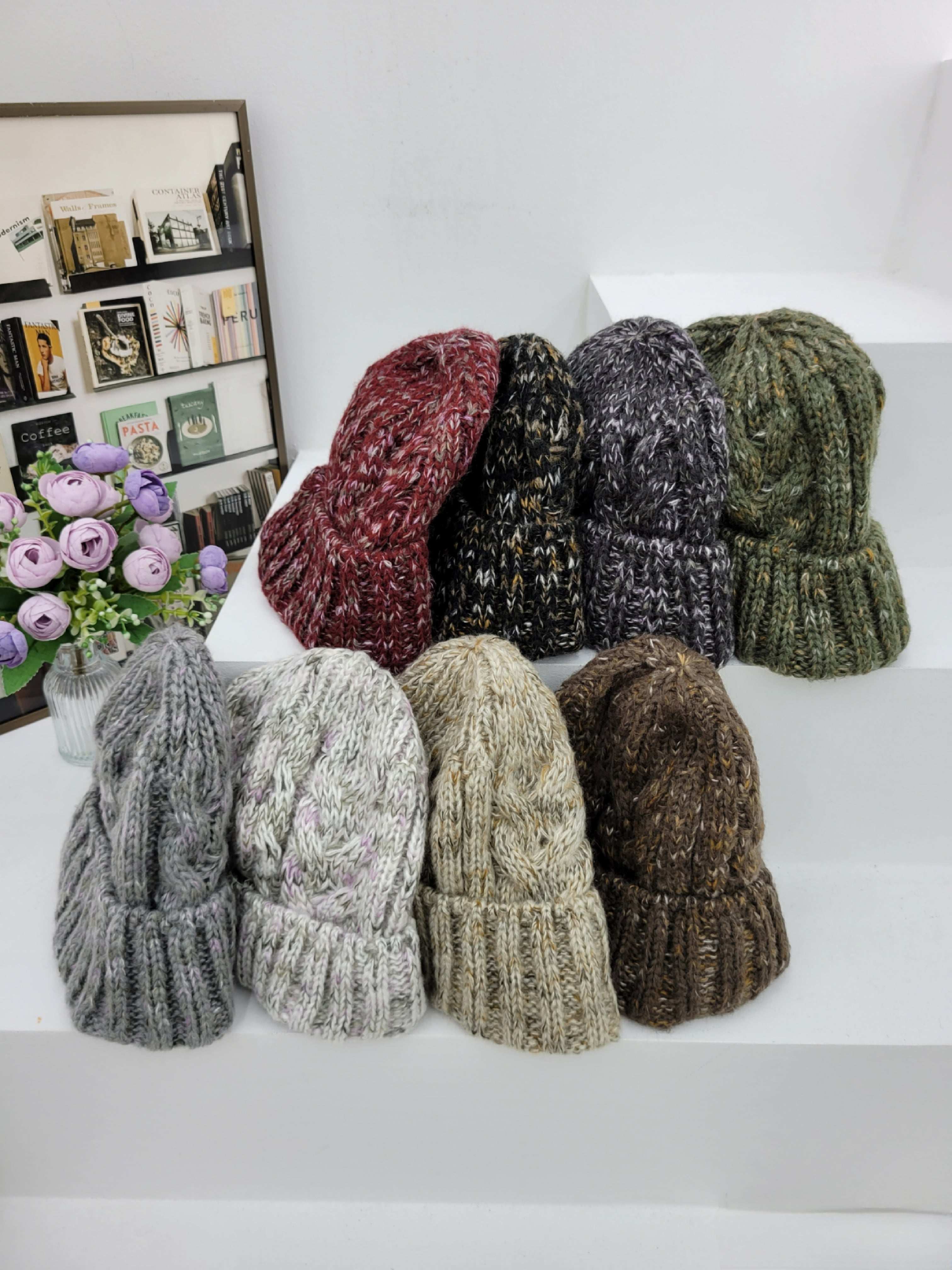 Collection of knit beanies in various colors on a white surface with a decorative background.