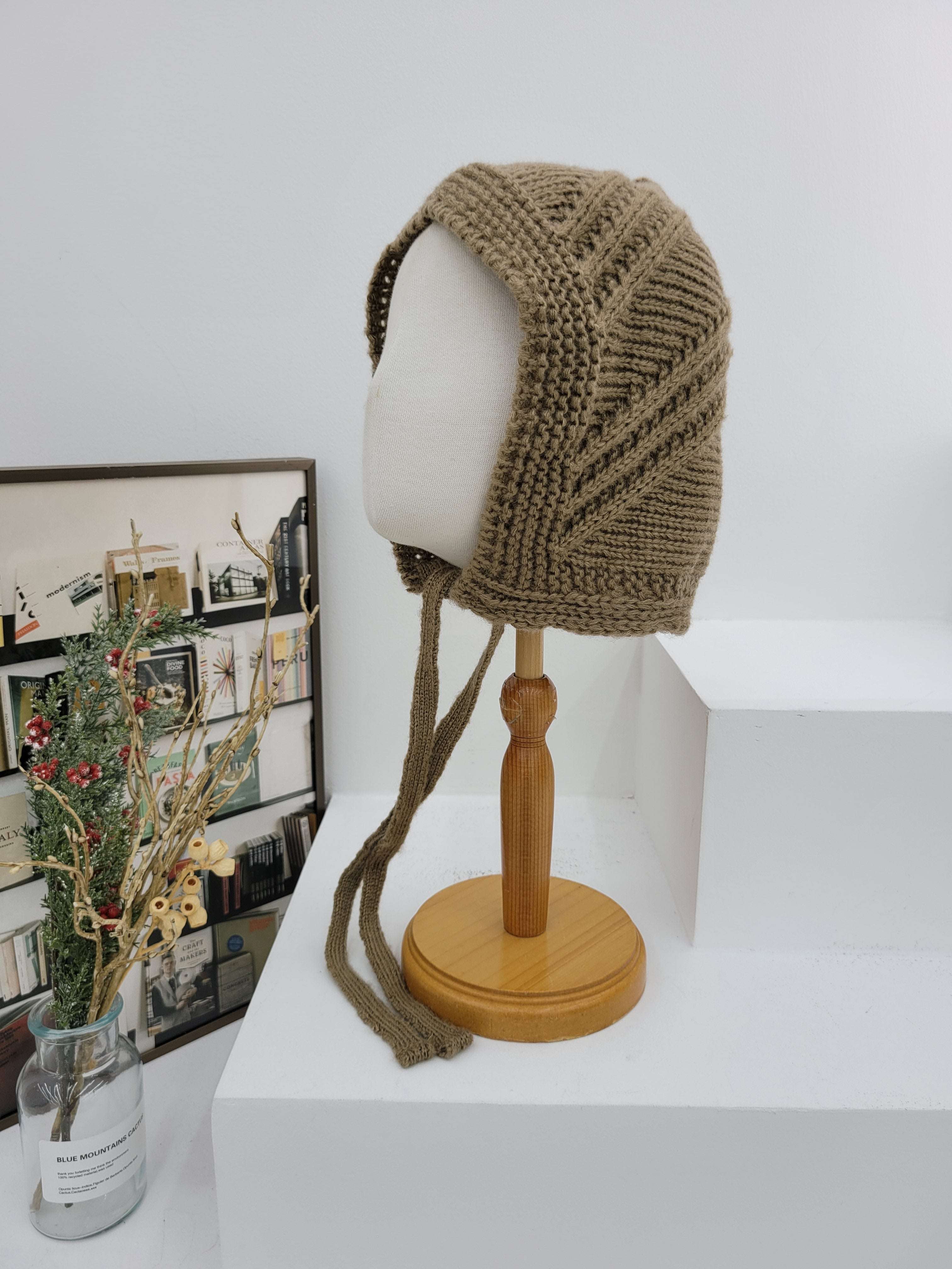 Knitted brown headband on a mannequin head with a wooden stand against a white background.