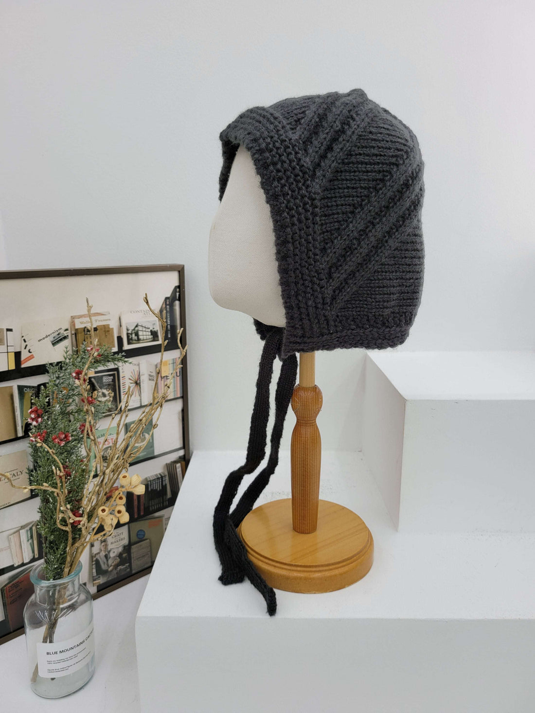 Knitted gray beanie on a mannequin head with a wooden stand against a white wall.