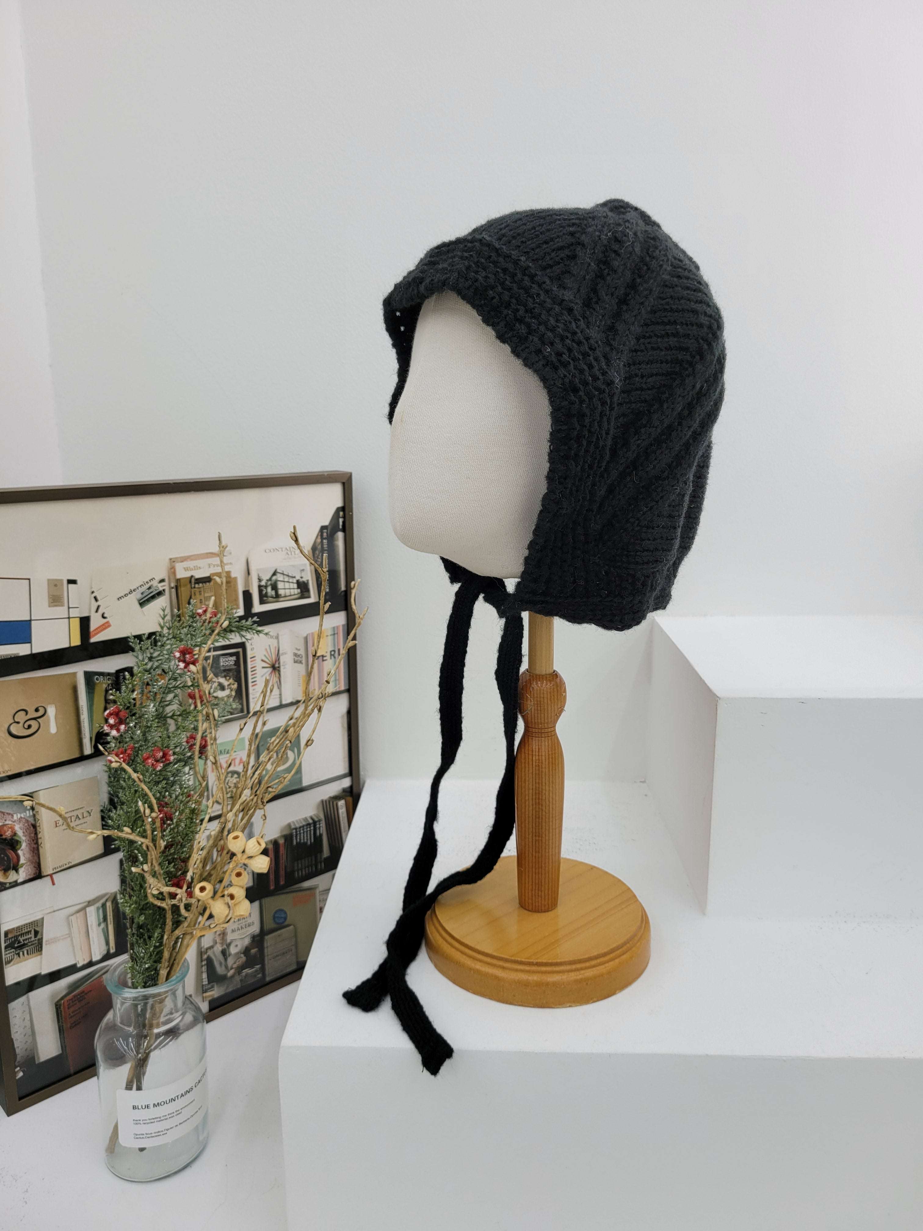 Black knitted hat on a mannequin head with a wooden lamp and photo album in the background.