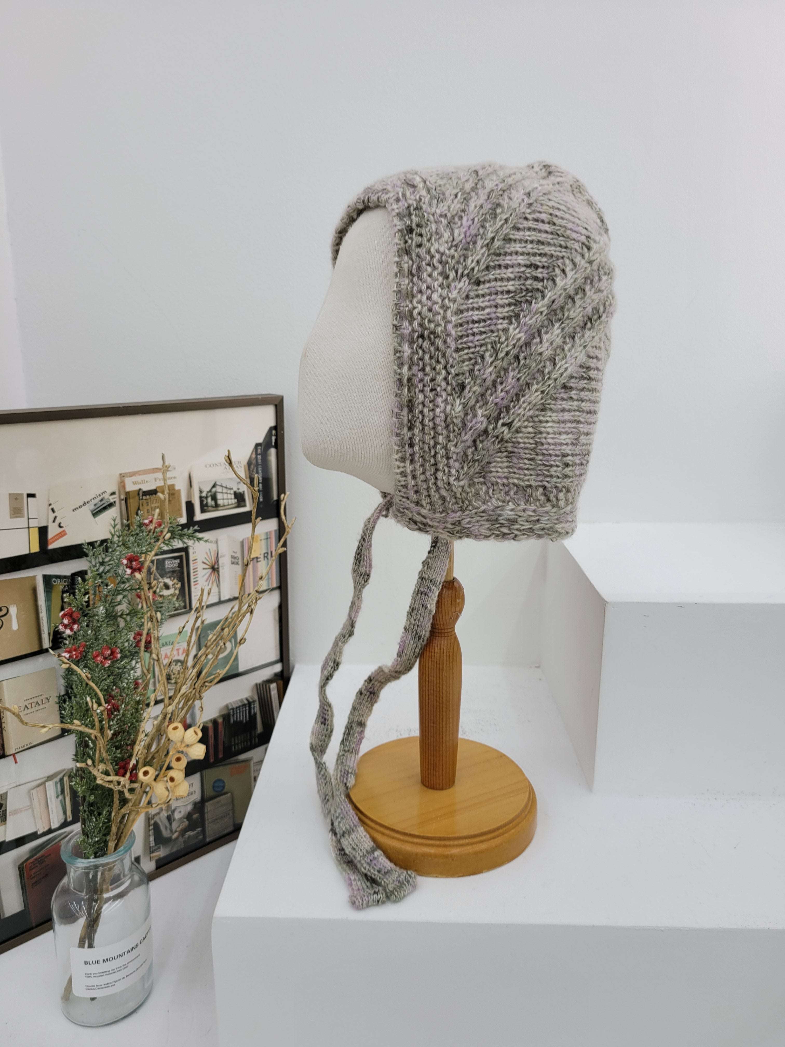 Knitted hat on a mannequin head against a white wall with a wooden rod and decorative items below.