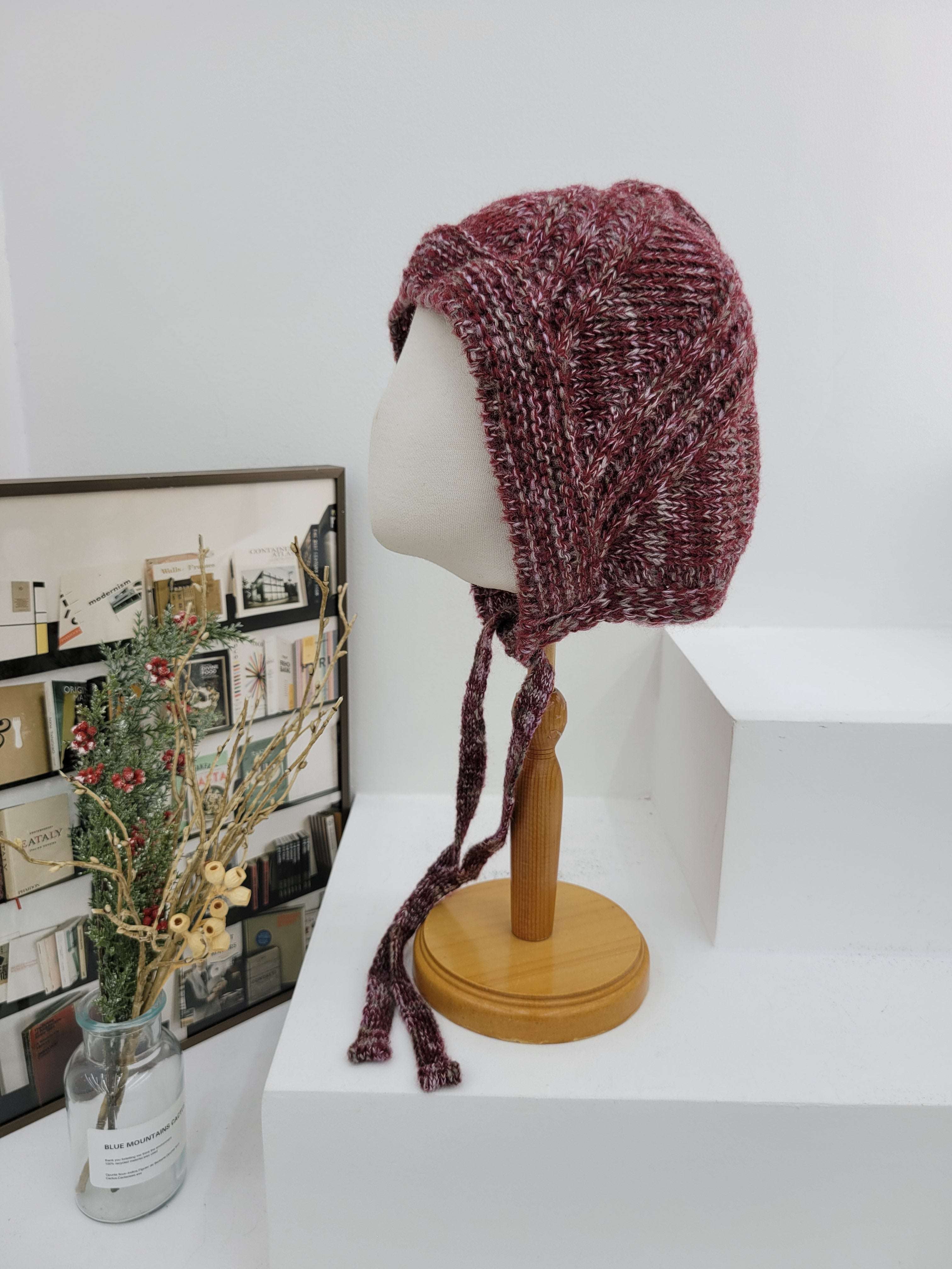 Knitted hat on a mannequin head against a white wall with a decorative frame in the background.
