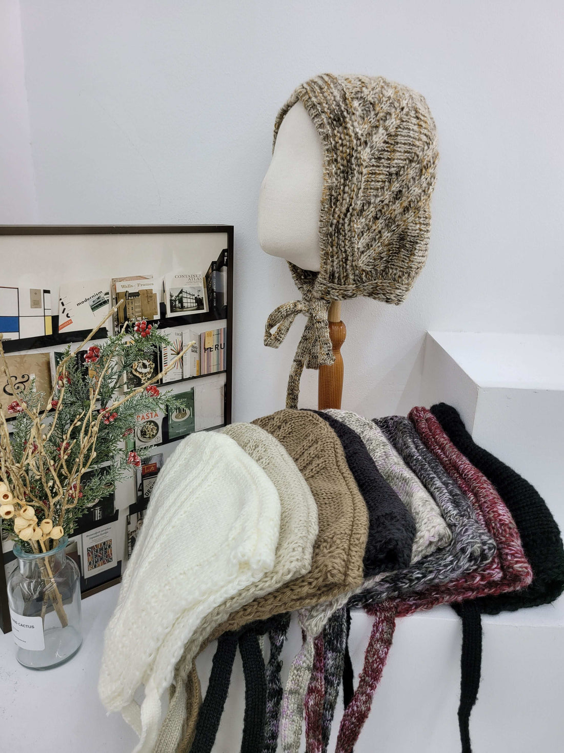 Collection of knitted hats on a mannequin and stacked against a white wall.