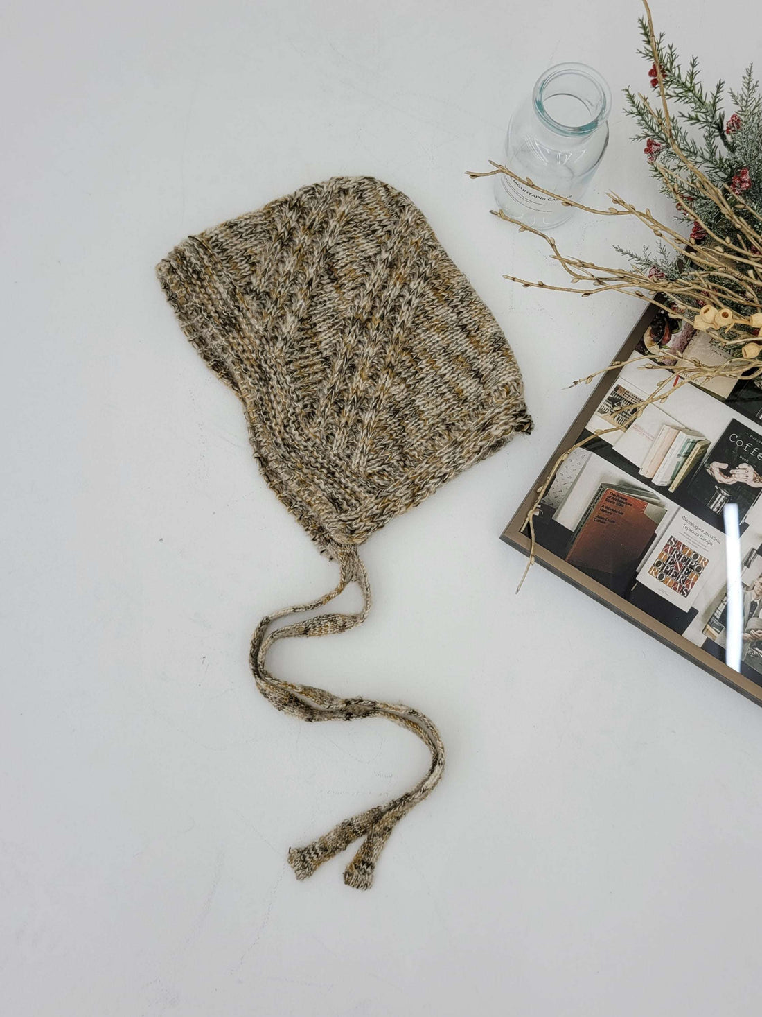 Knitted baby bonnet on a white surface with a book and decorative items.