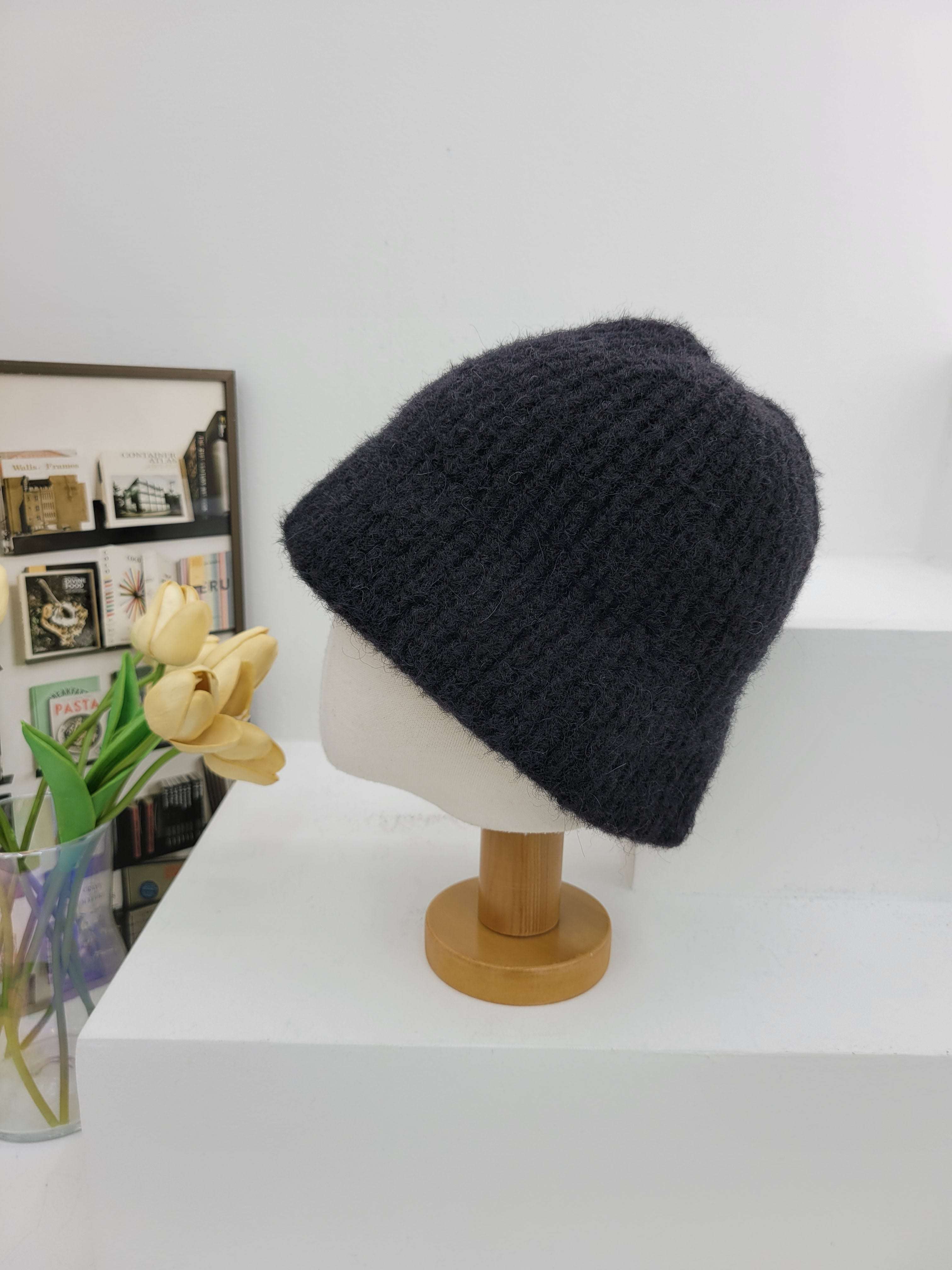 Black knit beanie on a mannequin head against a white wall with a decorative frame and flowers.