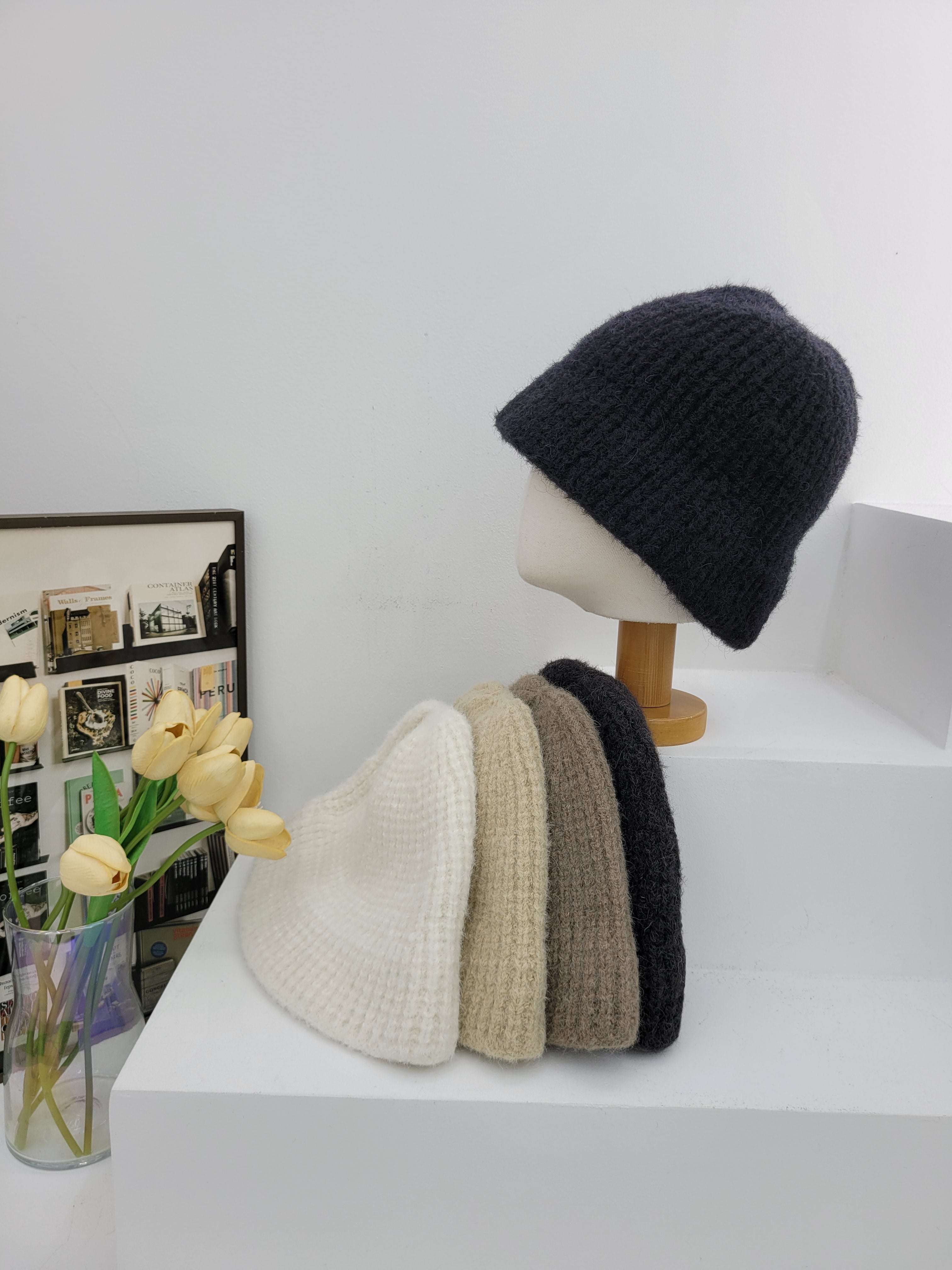 Black, brown, and beige beanies on a mannequin head against a white wall.